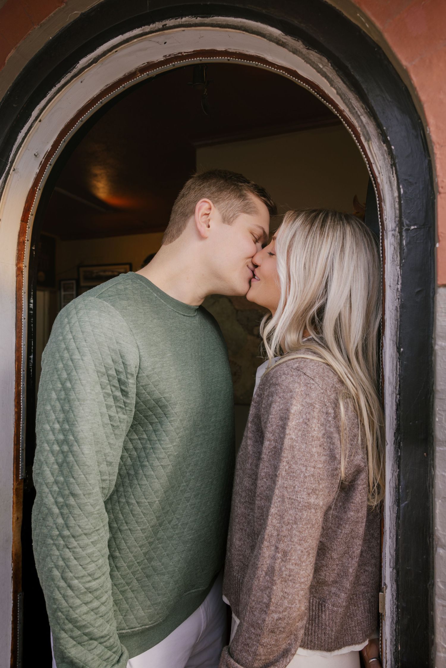 A couple embraces in a vintage arched doorframe with brick details.
