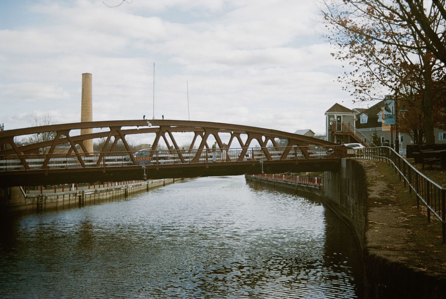 Historic bridge spans across a river with a tower and industrial smokestack in the background.