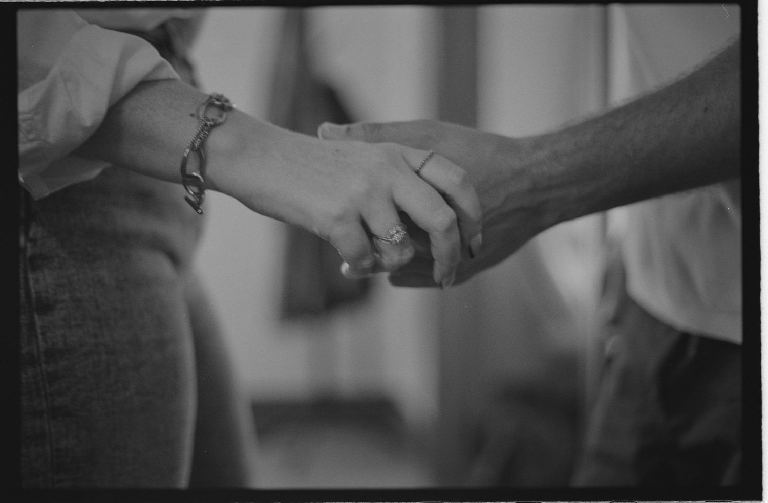 Black and white photo of two people holding hands, one wearing a bracelet and ring.