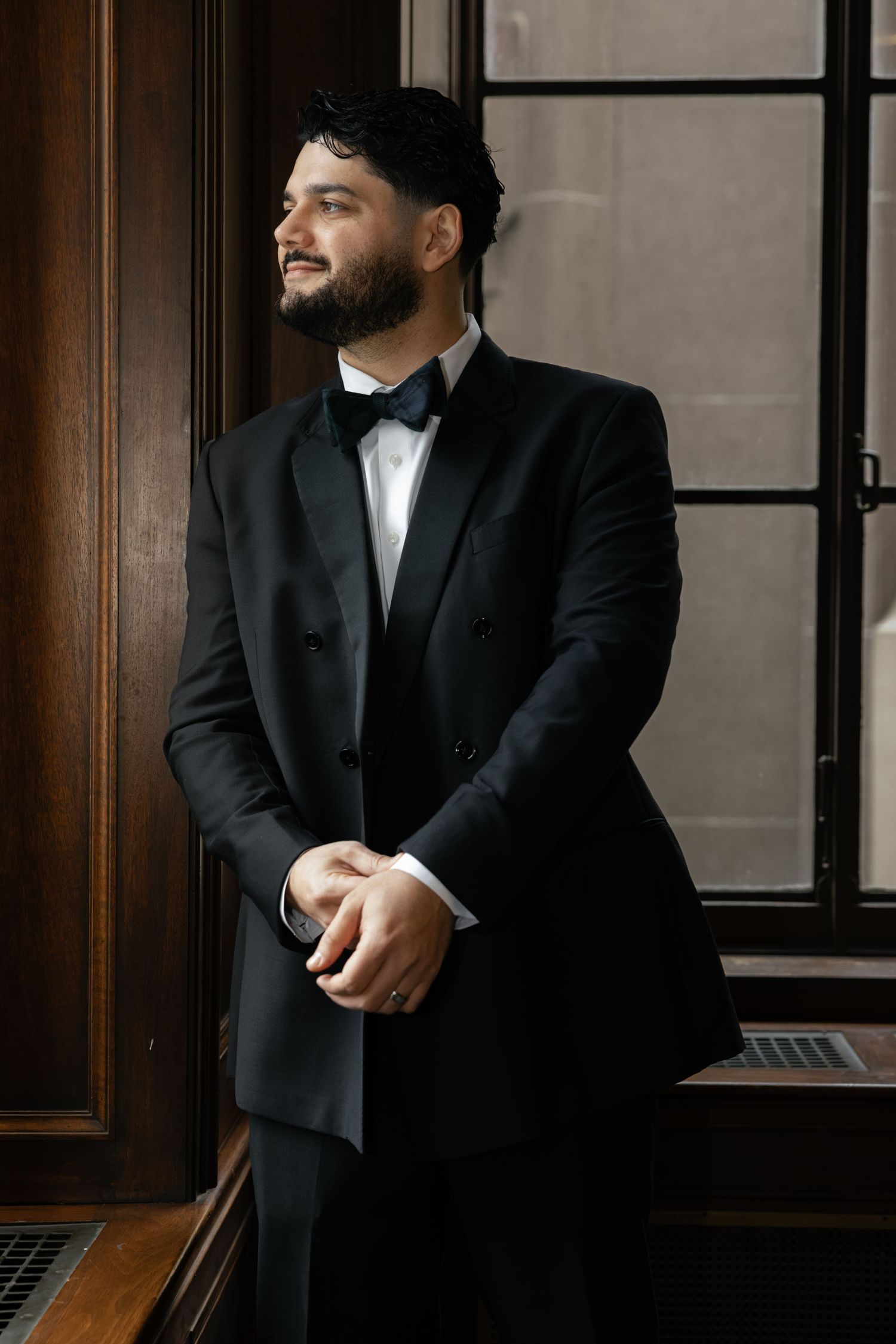 Groom in classic black tuxedo poses confidently in an elegant wood-paneled room. Arbor Midtown wedding photographer