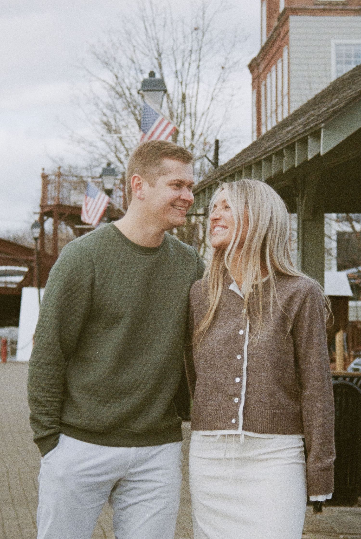A couple shares a joyful moment outdoors with American flags visible in the background.