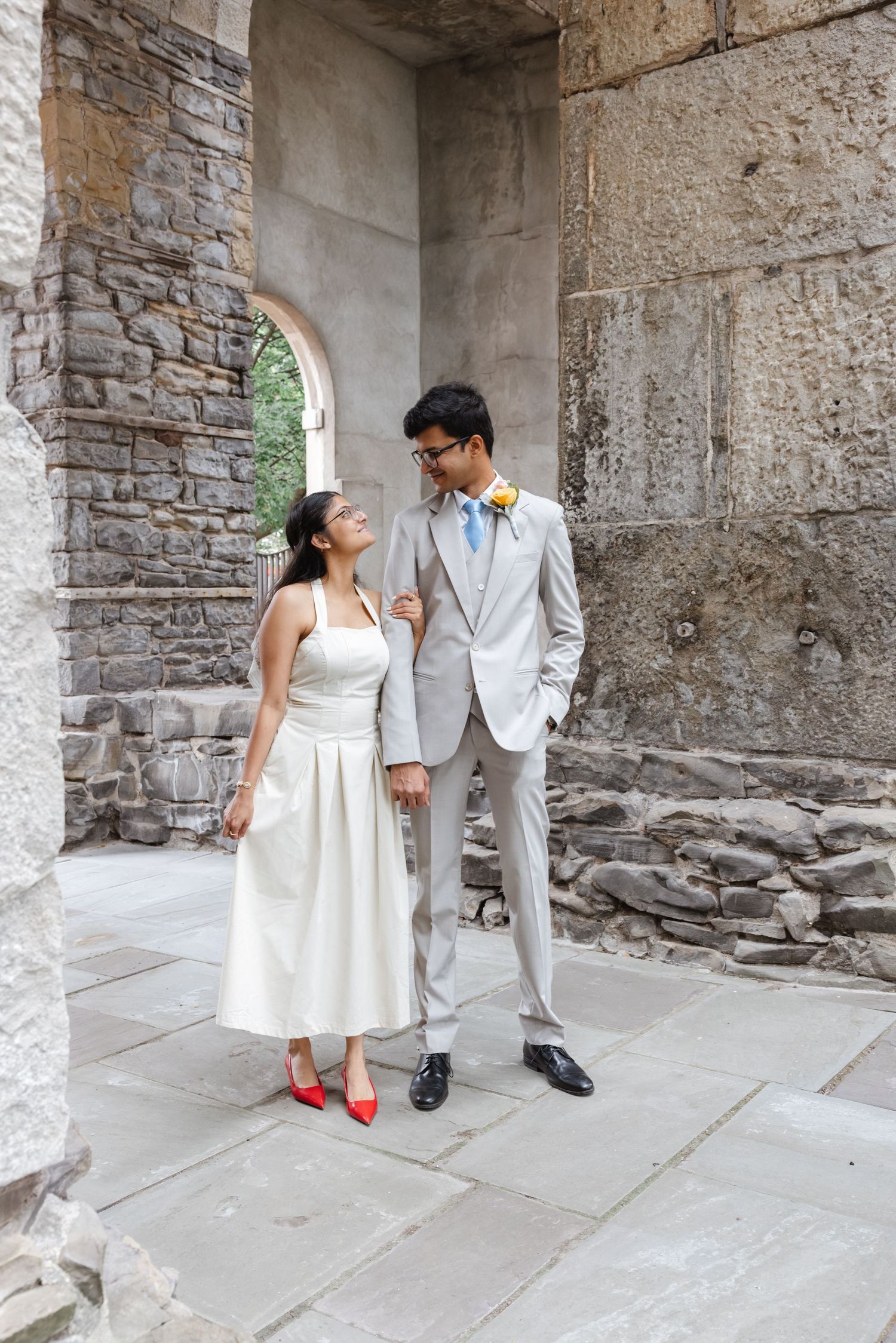A couple in white and gray formal attire posing against a stone archway. St. Josephs park wedding photographer