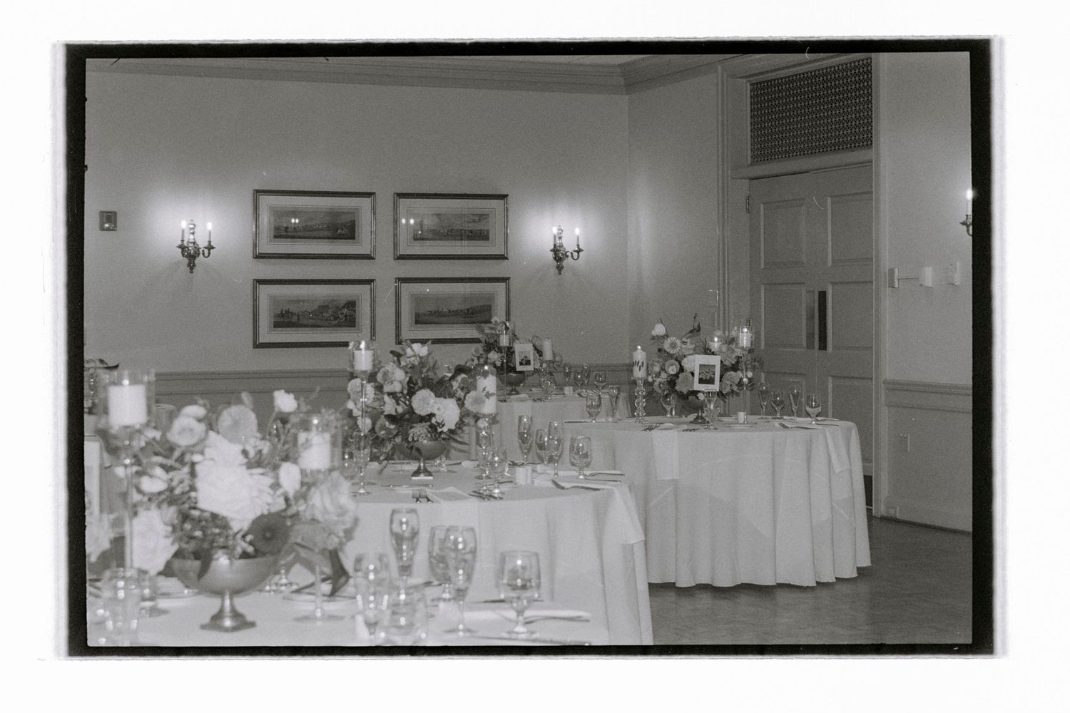 Black and white panoramic view of an elegant wedding reception hall setup with tables and decorations. Film wedding photographer NY