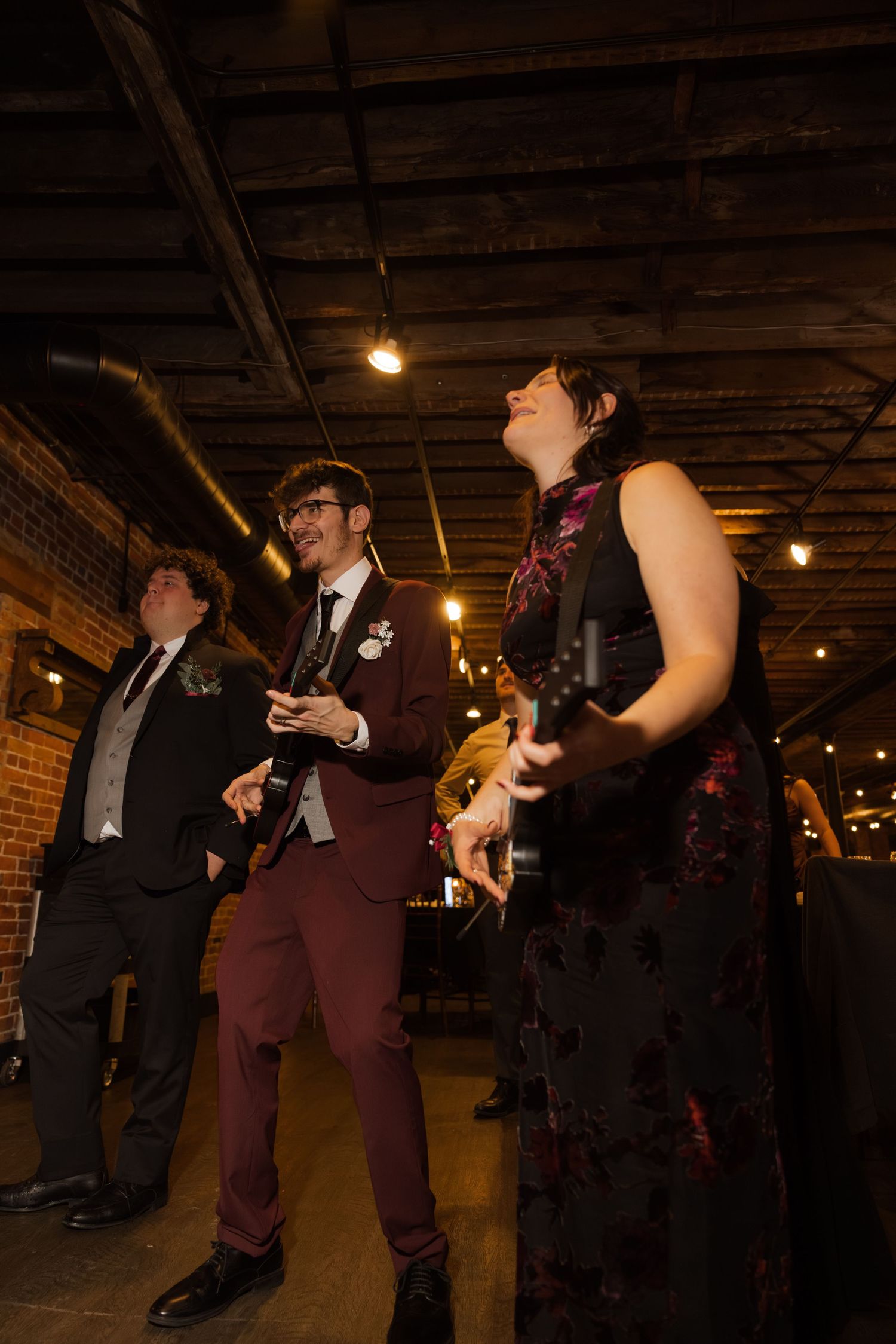 A group of people dressed in formal attire standing in a dimly lit room with hanging lights.