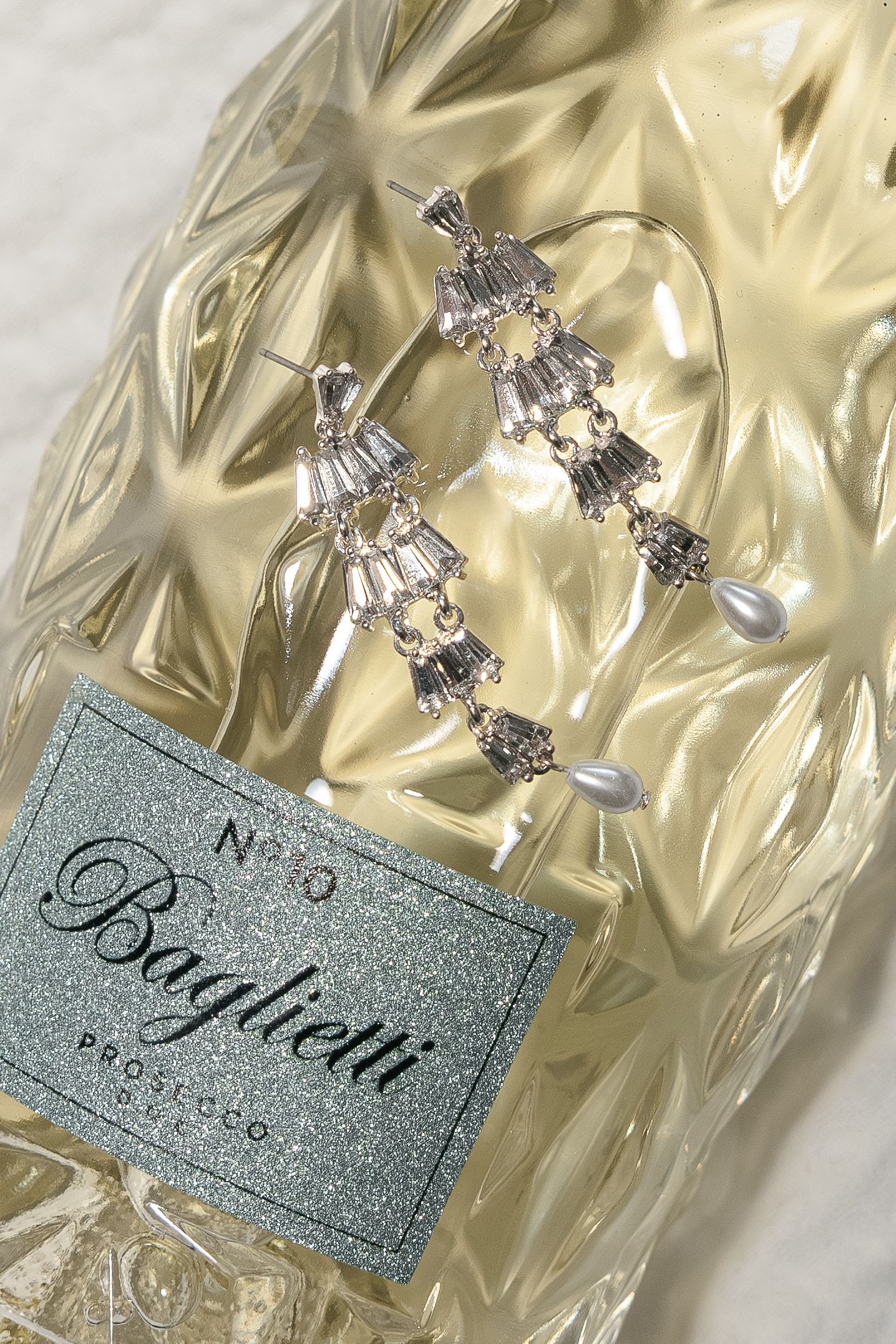 Luxury perfume bottles with silver caps and glittery labels displayed on a shimmering gold fabric background.