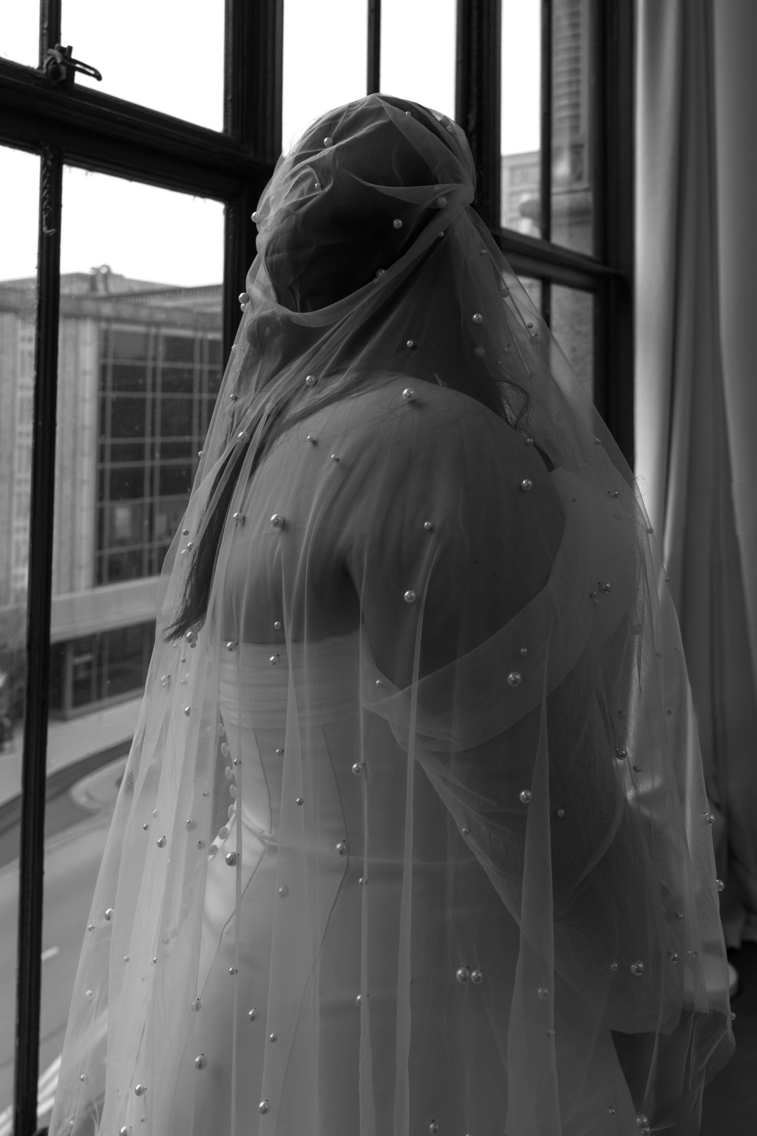 Silhouette of bride by window with pearl-adorned veil creating dreamy atmosphere. Arbor Midtown wedding photographer