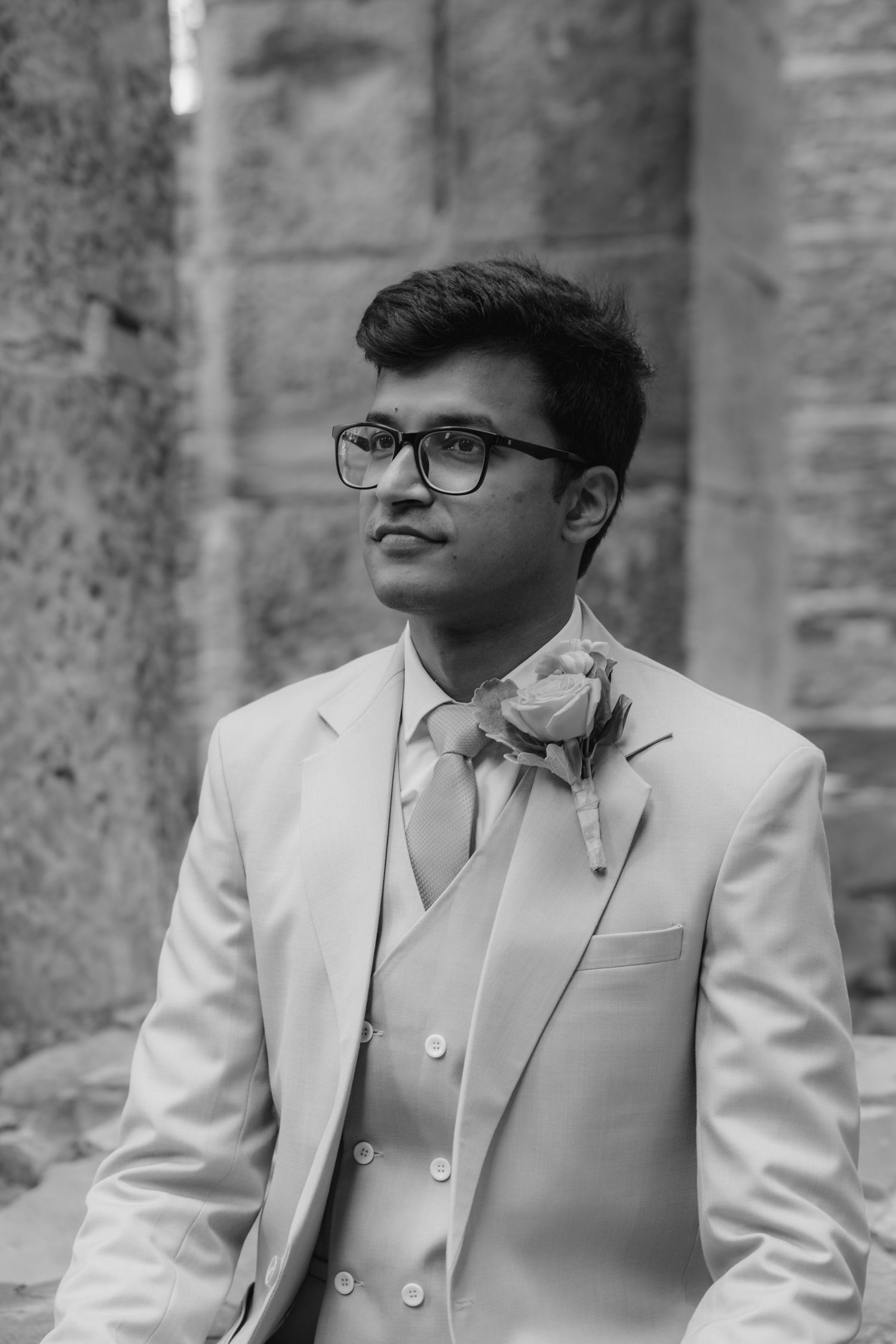 A portrait in black and white showing formal attire and glasses against a stone backdrop.  St. Josephs park wedding photographer