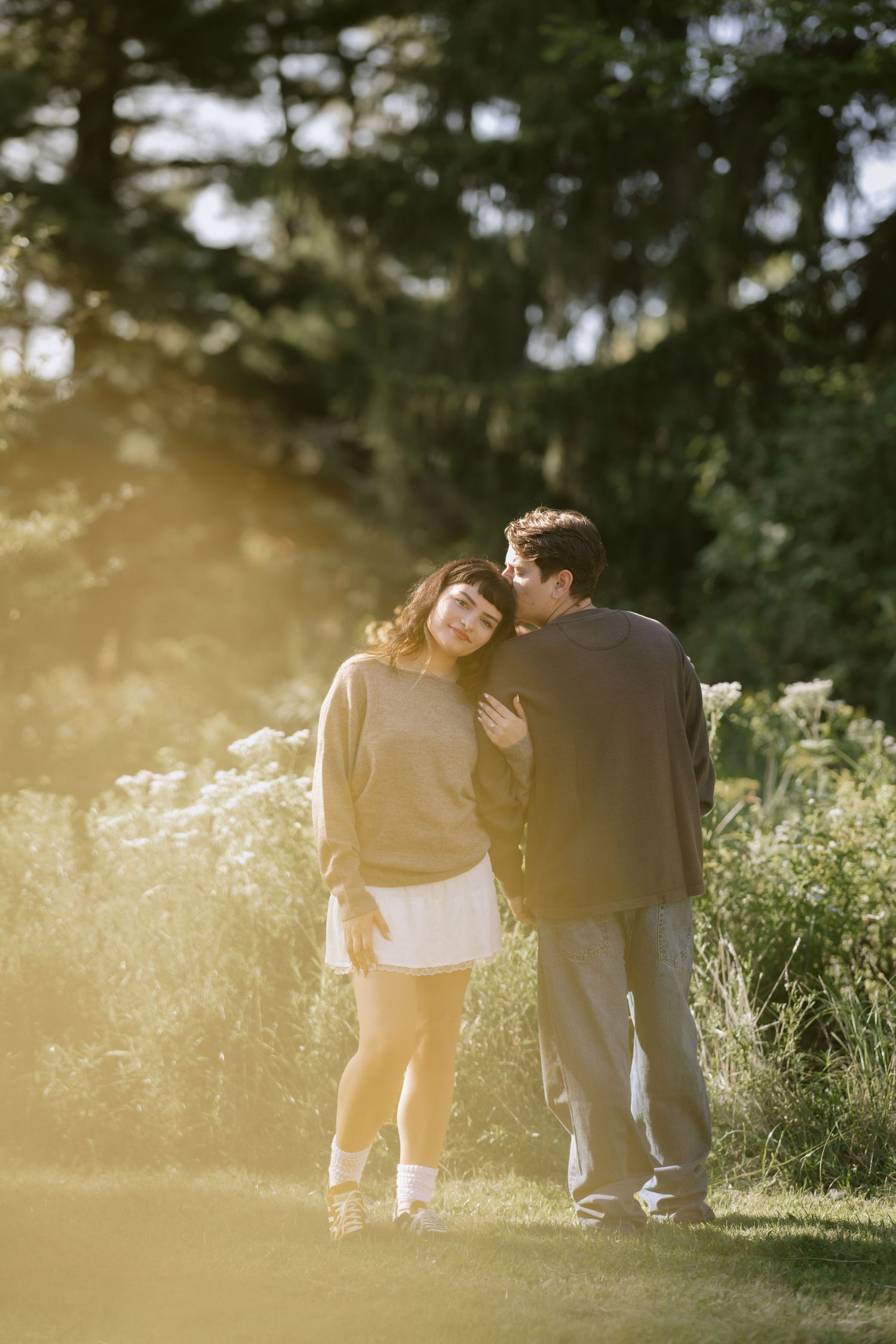 A couple shares a romantic moment in a sun-drenched meadow at golden hour. Rochester NY documentary engagement photography