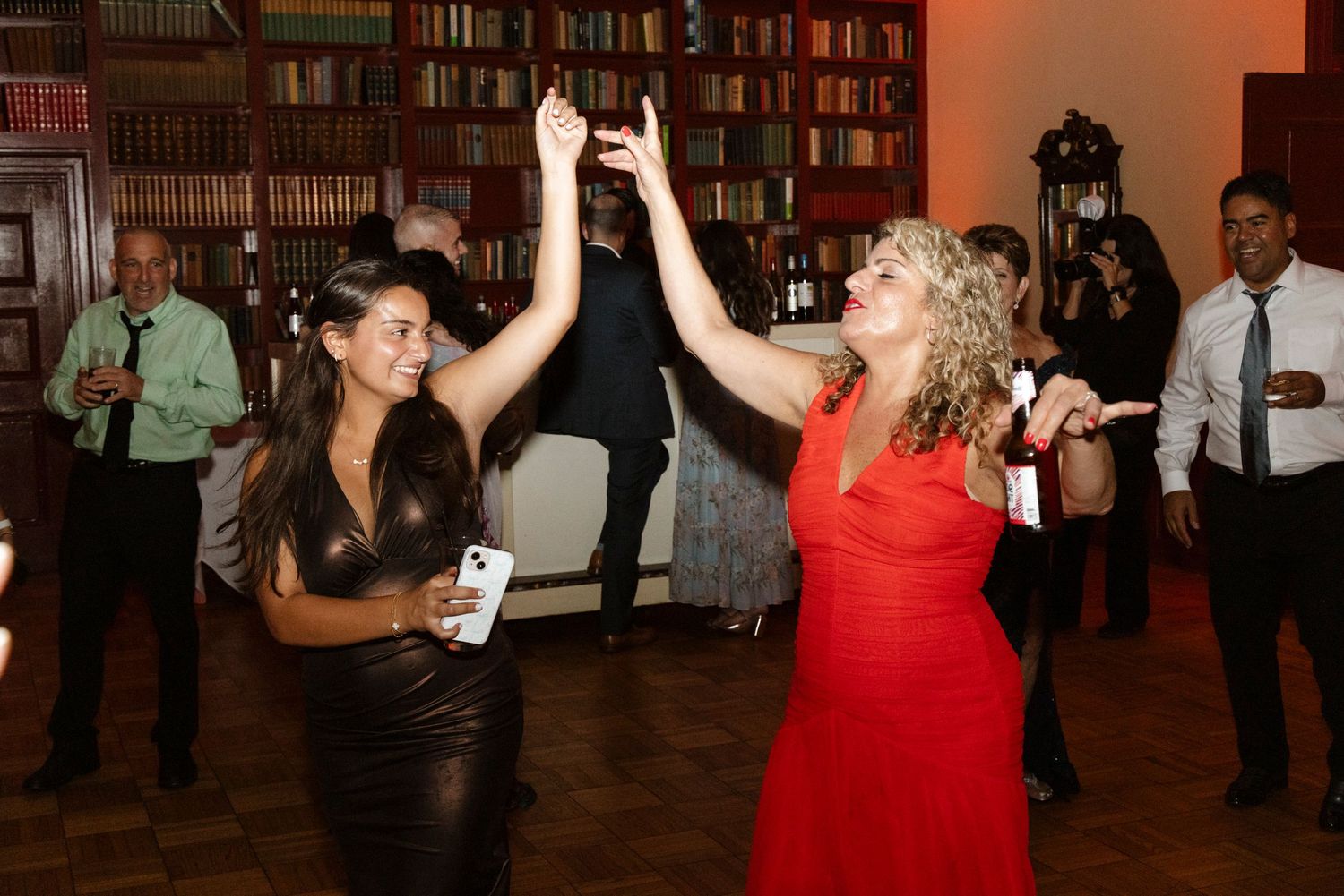 Wedding reception guests dancing & celebrating on a dance floor with bookshelves in the background. Rochester NY candid wedding photography