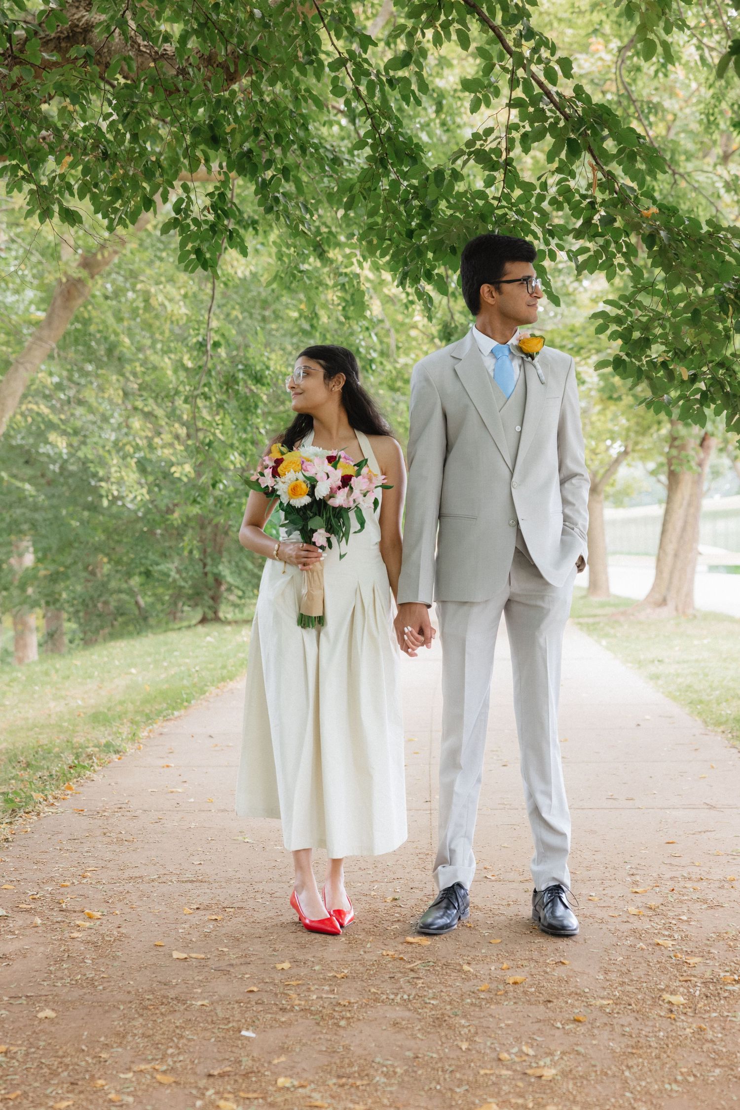 Wedding couple walking along a tree-lined path, showing their colorful shoes. Highland park conservatory wedding photographer