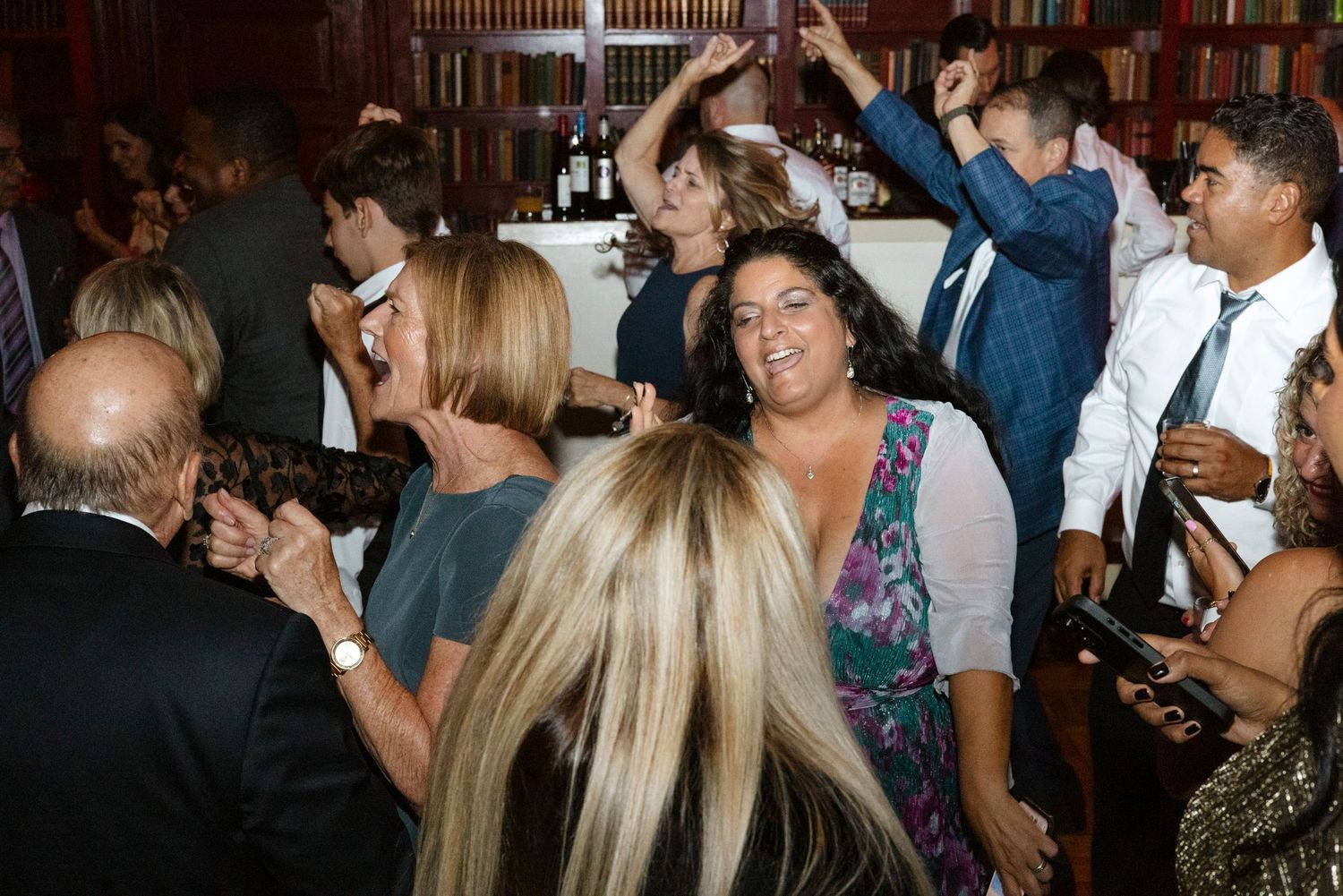 Crowded dance floor with party guests enjoying themselves in library setting. Rochester NY documentary wedding photography