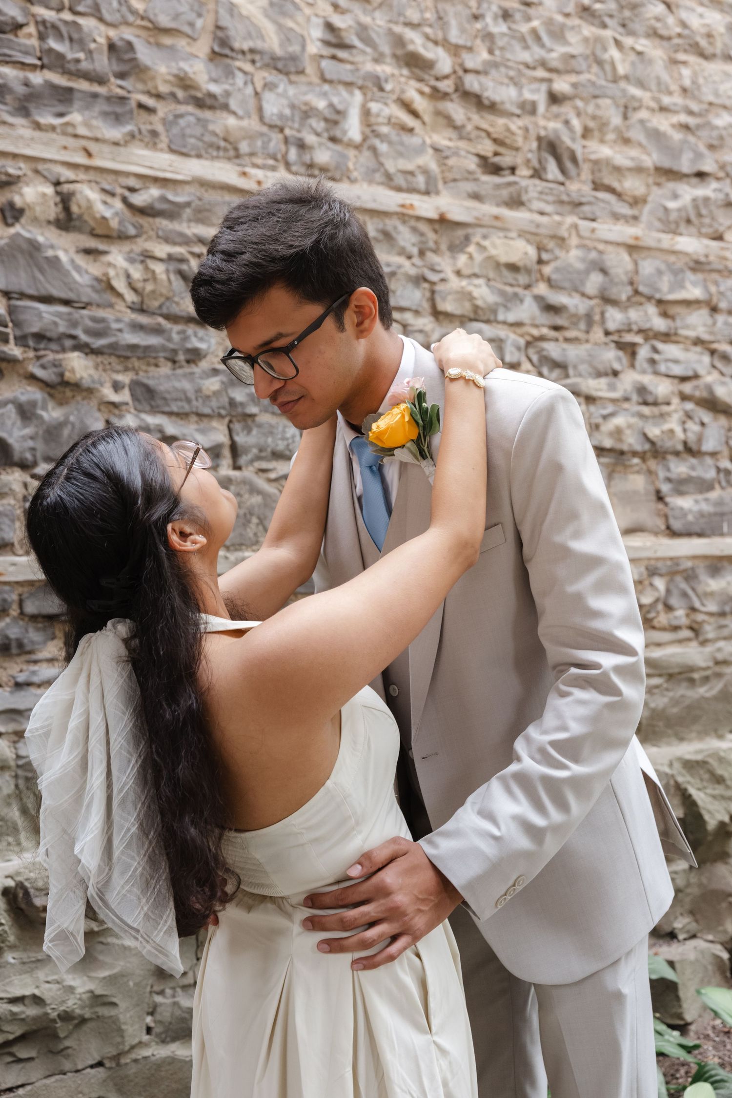 A romantic moment captured against a rustic stone wall backdrop with yellow floral accents.  St. Josephs park wedding photographer