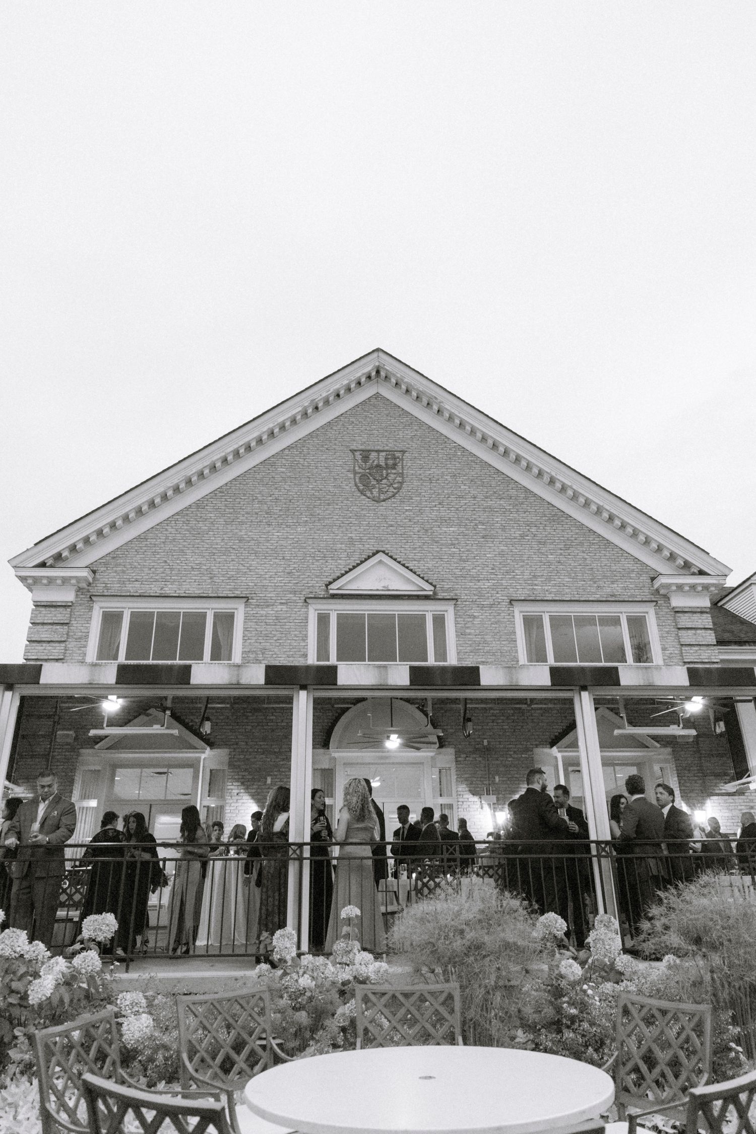 Exterior view of a brick building with white columns and guests gathered on the patio. Rochester NY documentary wedding photography