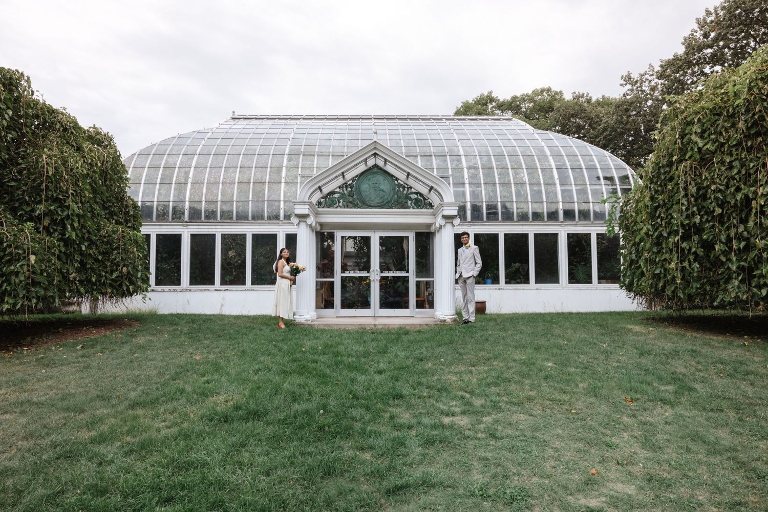 Exterior view of a large greenhouse and conservatory building with manicured lawns.  Rochester conservatory wedding photographer