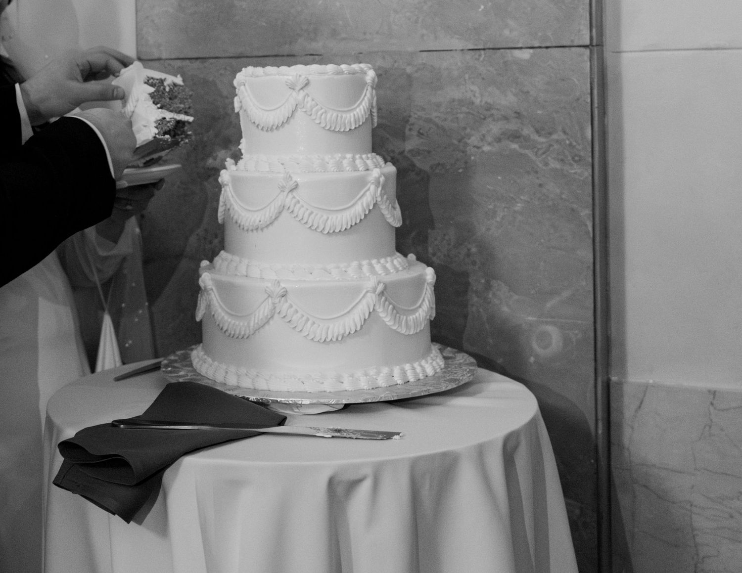 Classic white tiered wedding cake with elegant piped decorations displayed at reception. . Arbor Midtown wedding photographer