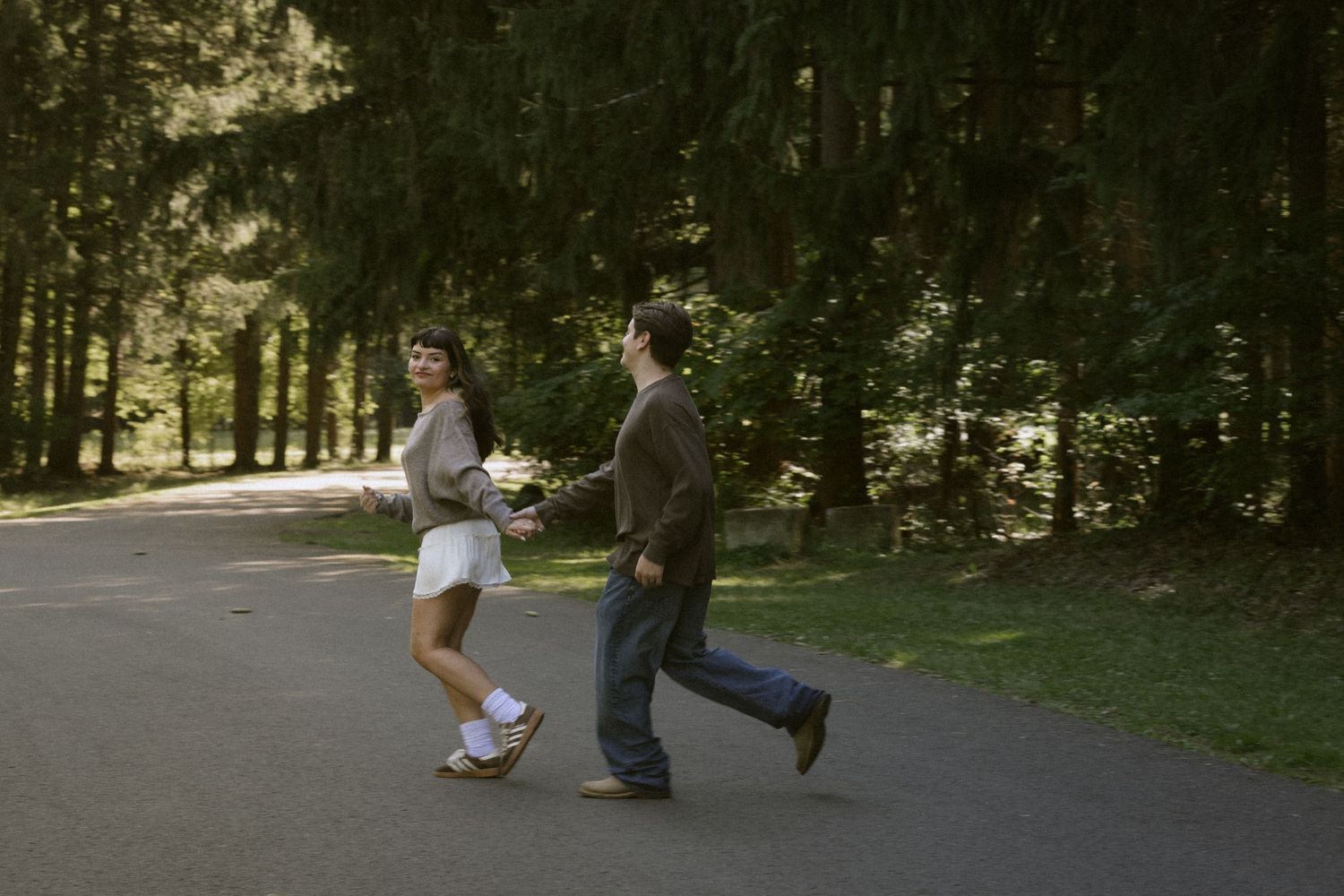 Couple walking together on a tree-lined path in a park. Rochester NY documentary engagement photography