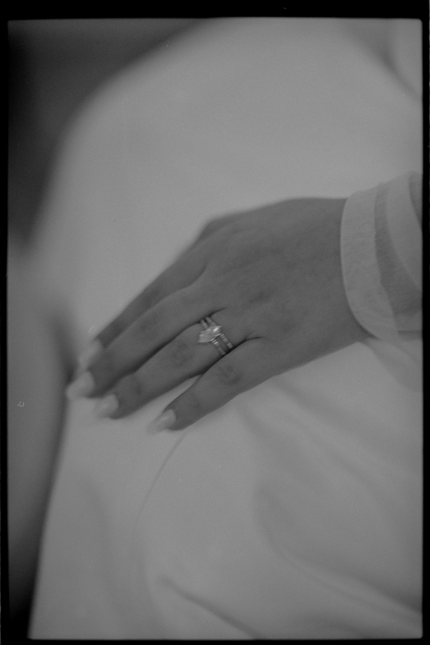 Black and white photo of an engagement ring on a hand against white fabric.
