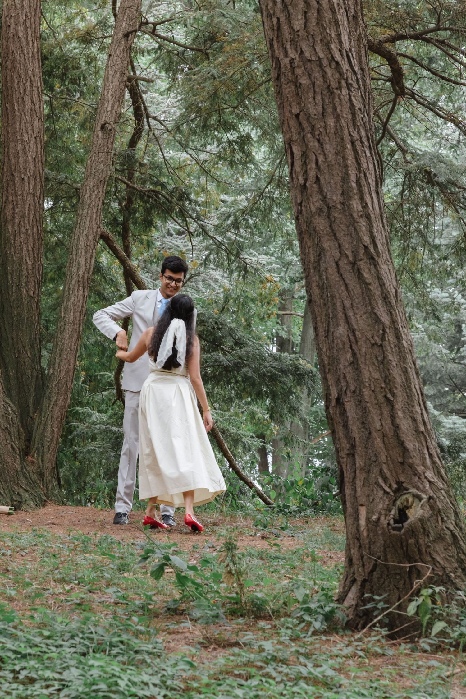 Playful moments captured between a couple in formal wear among pine trees. Rochester conservatory elopement photographer