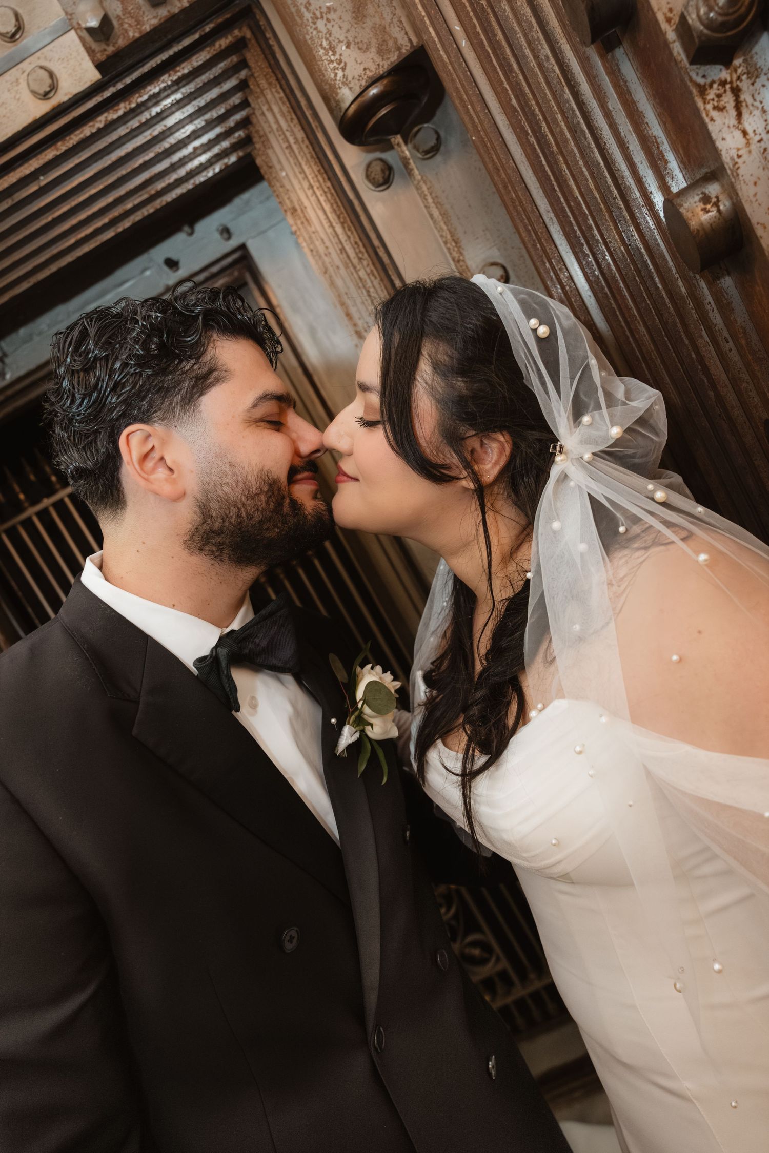 A bride and groom share a loving kiss in a rustic, wooden setting on their wedding day.