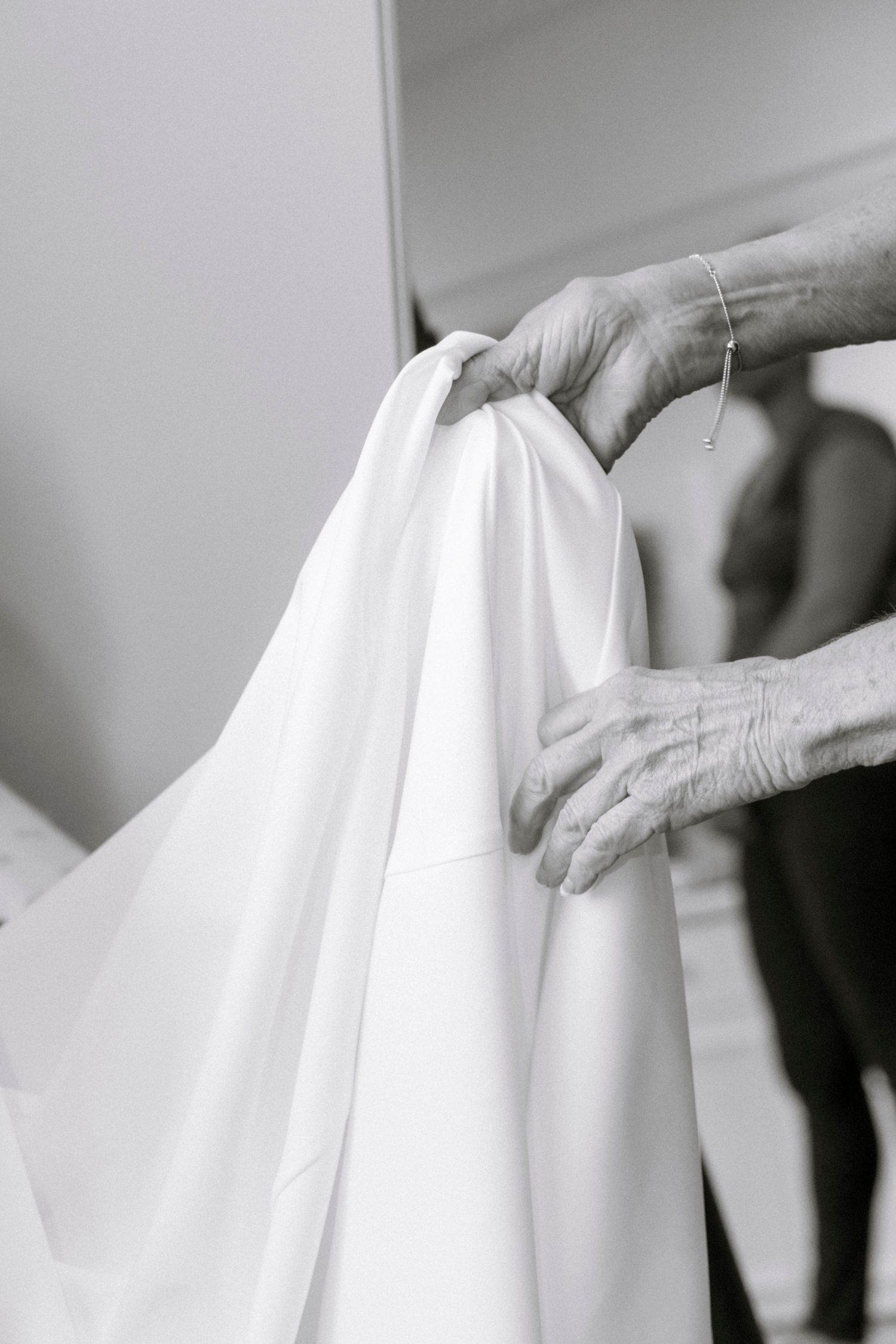 Close-up detail of hands adjusting the fabric of a white wedding dress.Rochester NY documentary wedding photography