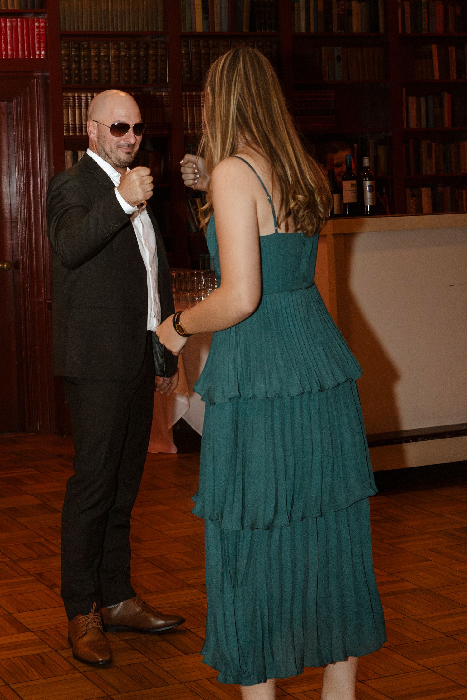 Dancing couple in formal attire, with woman wearing teal dress in library setting. Rochester NY documentary wedding photography