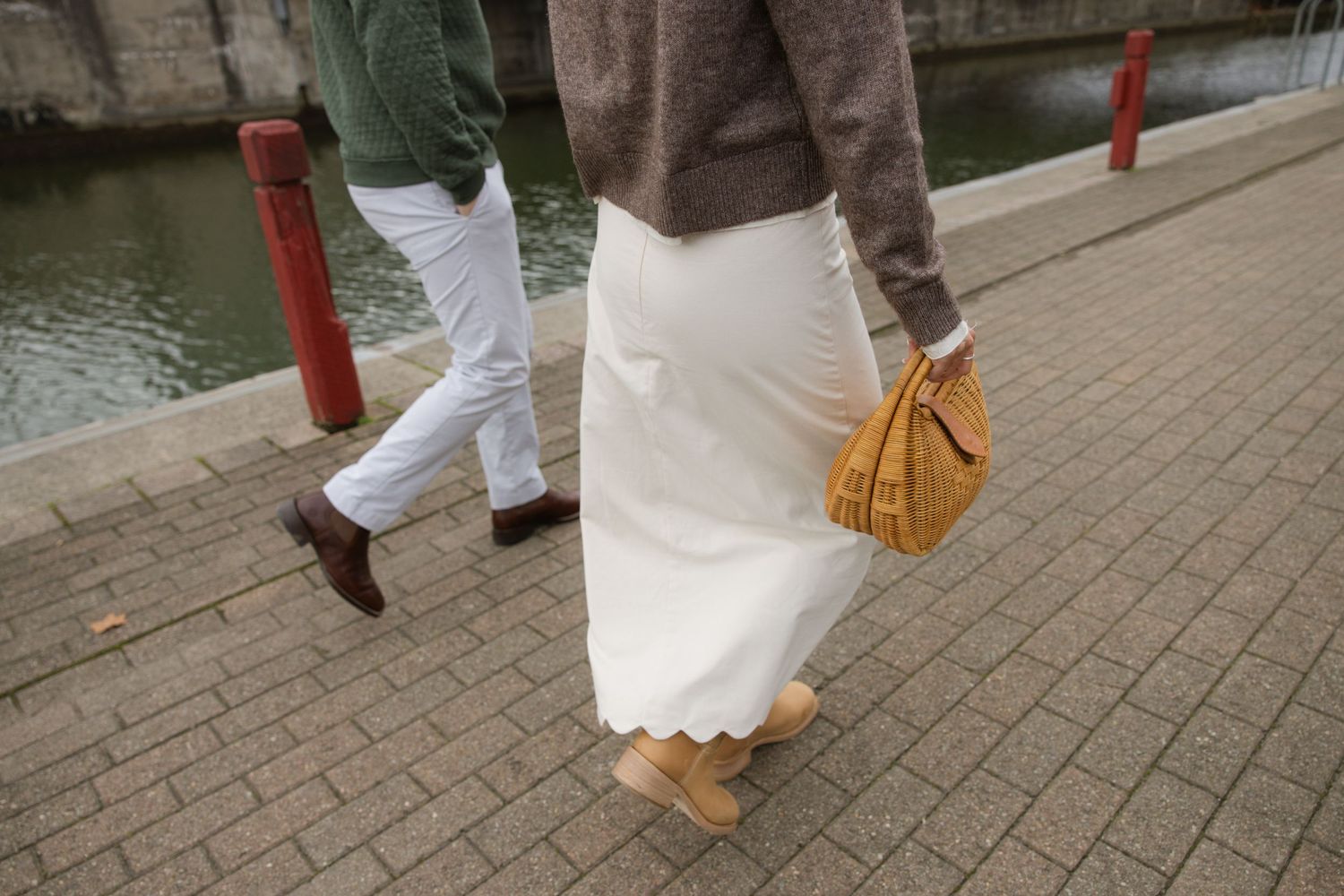 Close-up of white pants and brown sweater outfits with a tan handbag on a riverside walkway. Film wedding photographer Rochester  NY