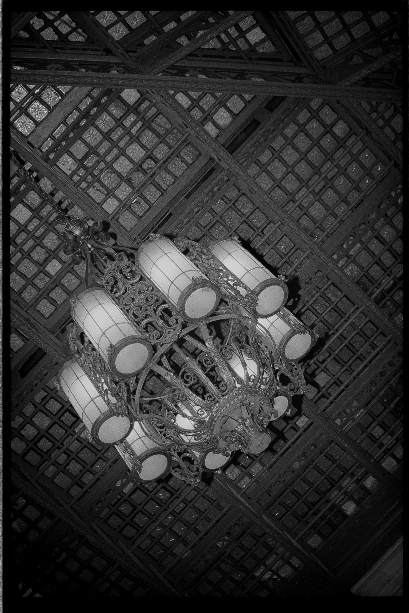 A black and white image of a decorative light fixture with intricate metalwork and multiple bulbs suspended from a latticed ceiling.