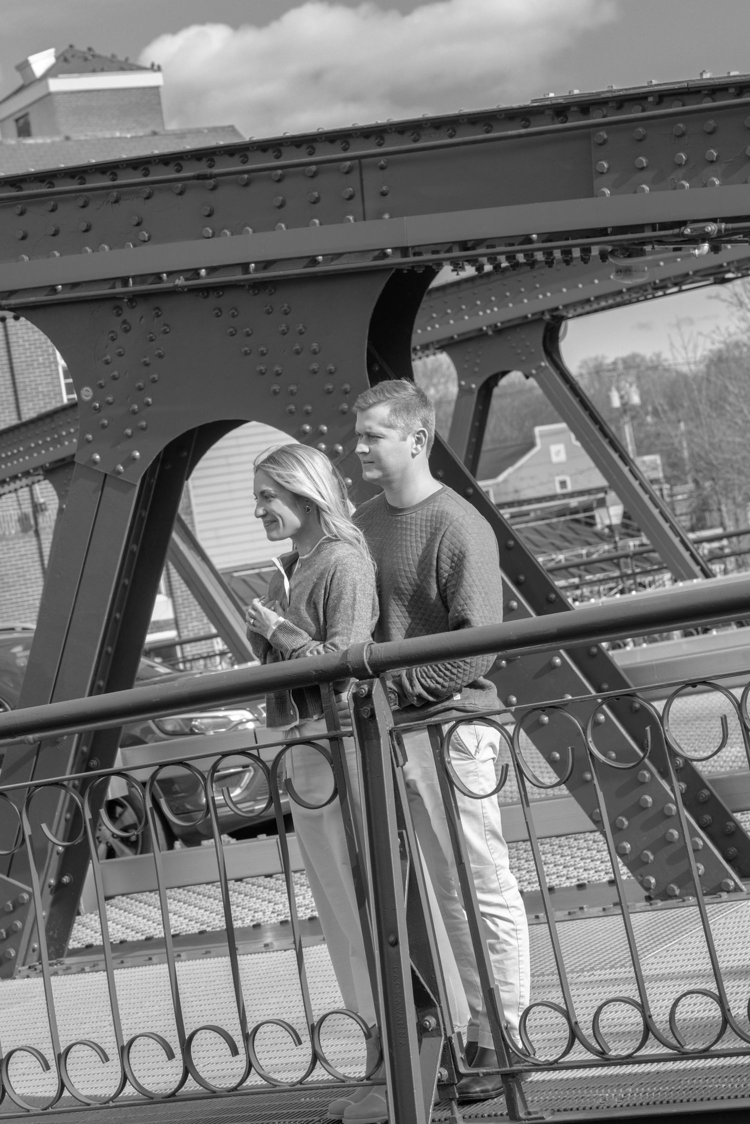 A couple stands on a metal bridge in black and white photography. Film wedding photographer Rochester  NY