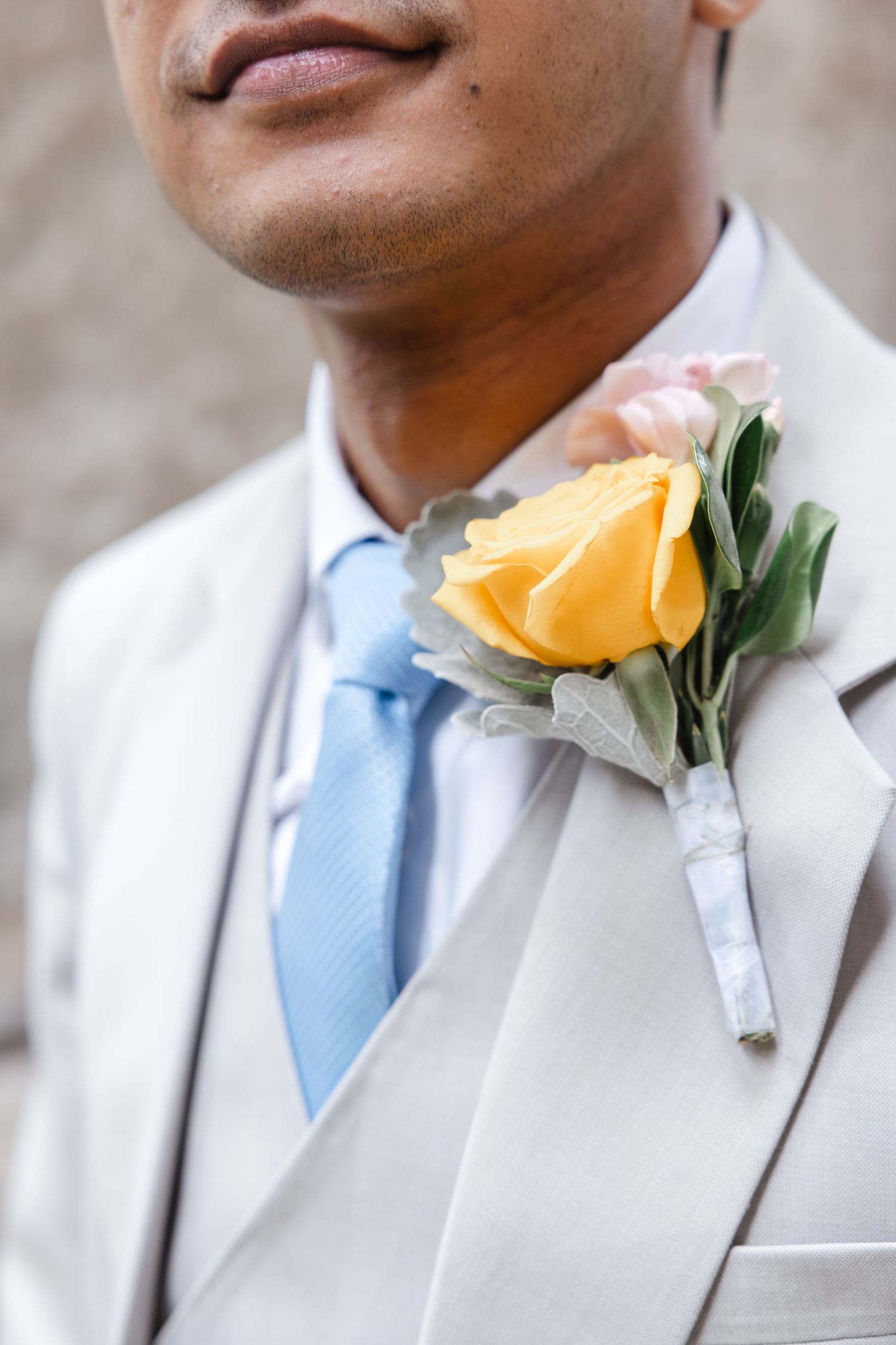 Close-up of a yellow rose boutonniere on a light grey suit with blue tie.  St. Josephs park wedding photographer