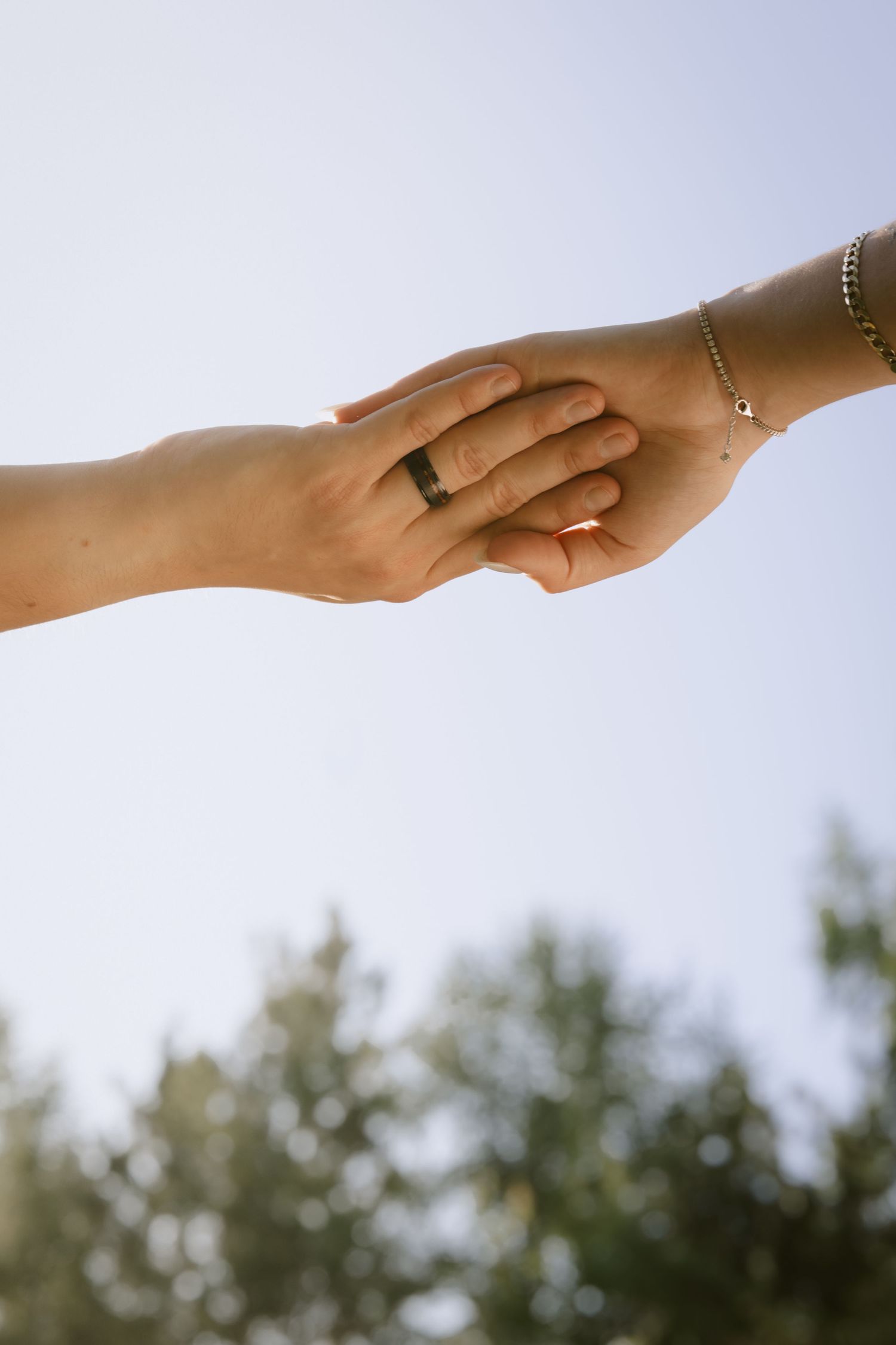 Two hands clasped together against a bright sky with delicate jewelry visible.  Rochester NY film engagement photography