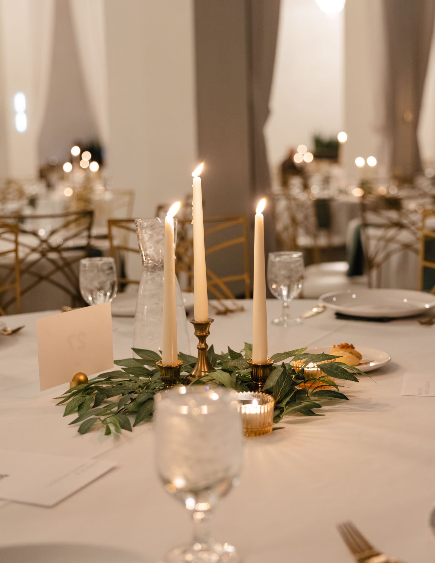 Romantic table setting with white taper candles, greenery, and place settings for wedding dinner. . Arbor Midtown wedding photographer