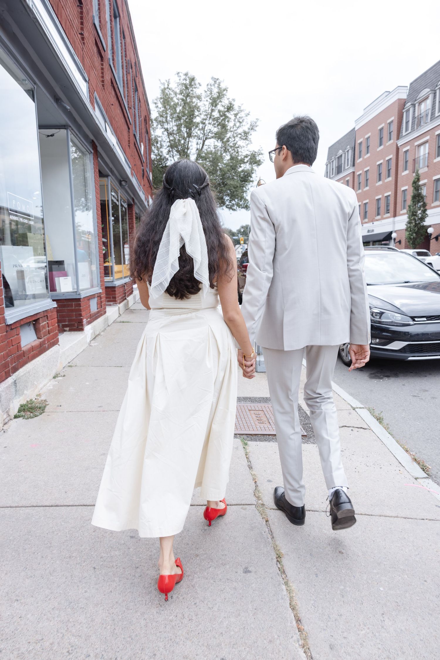 A couple in white and gray outfits walk hand in hand down a city sidewalk.  Fun elopement photography Rochester NY