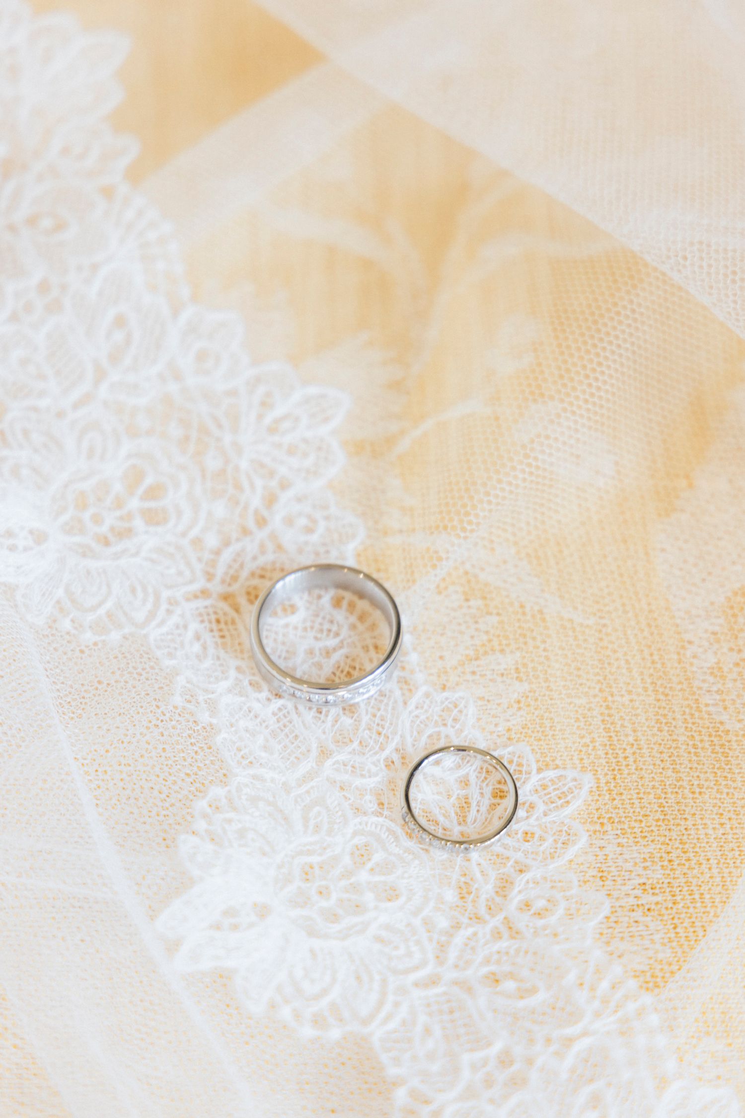 Wedding rings rest delicately on white lace fabric, creating an elegant bridal detail shot.Rochester NY documentary wedding photography