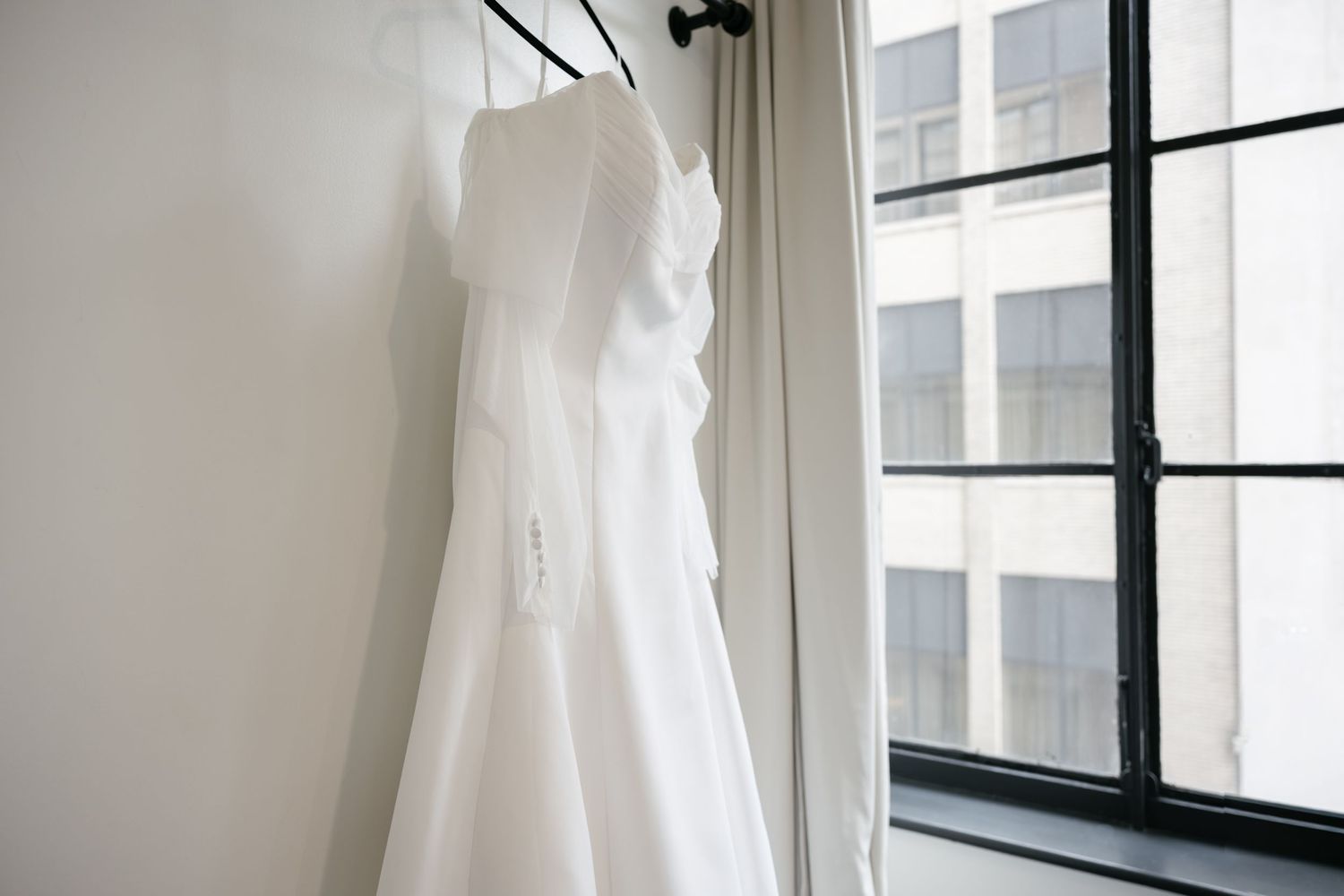 White wedding dress hanging by window with natural light streaming in.