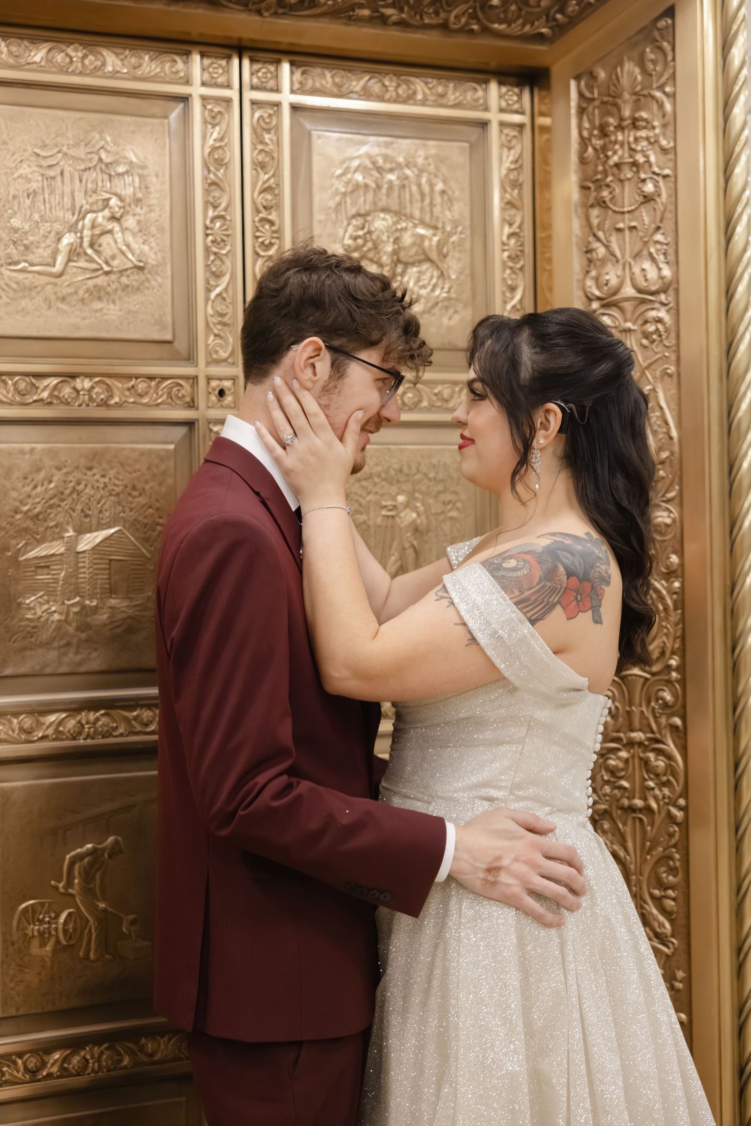 A romantic wedding couple embraces against an ornate gold-toned wall with decorative relief panels.