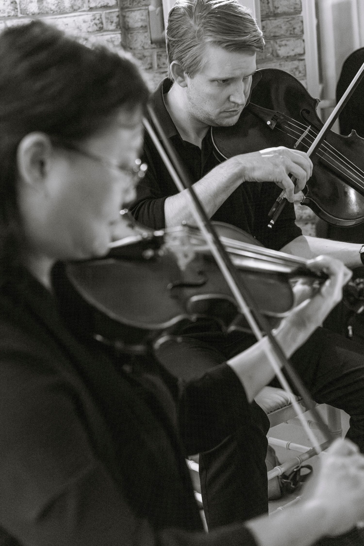 Musicians playing violins in formal black attire at an event. Rochester NY documentary wedding photography