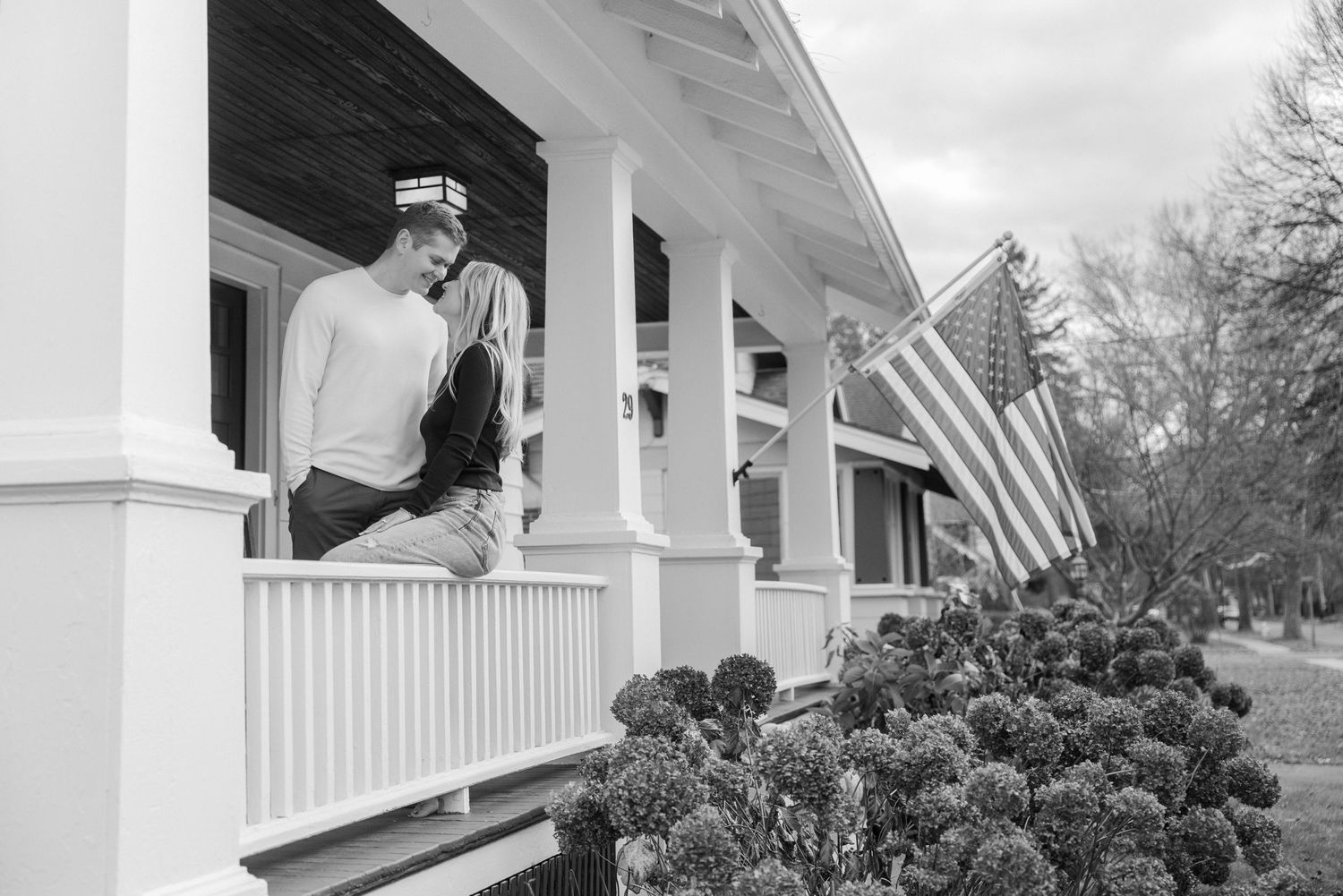 White pillars of a front porch with autumn decorations and an American flag. Fairport NY home engagement photography