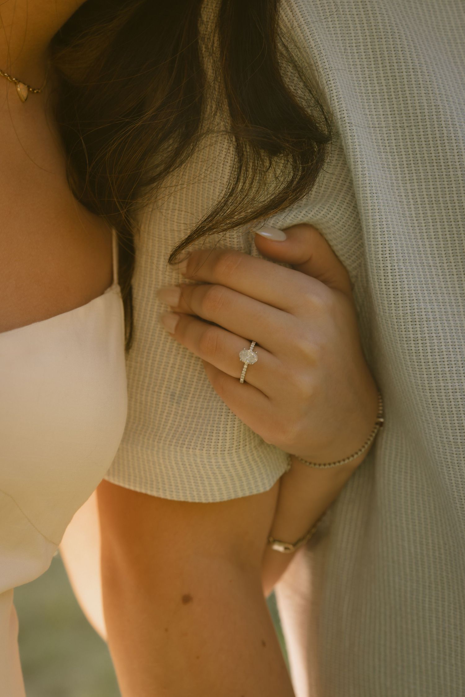Close-up of an engagement ring on a hand against a white sweater in natural lighting.  Rochester NY film engagement photography