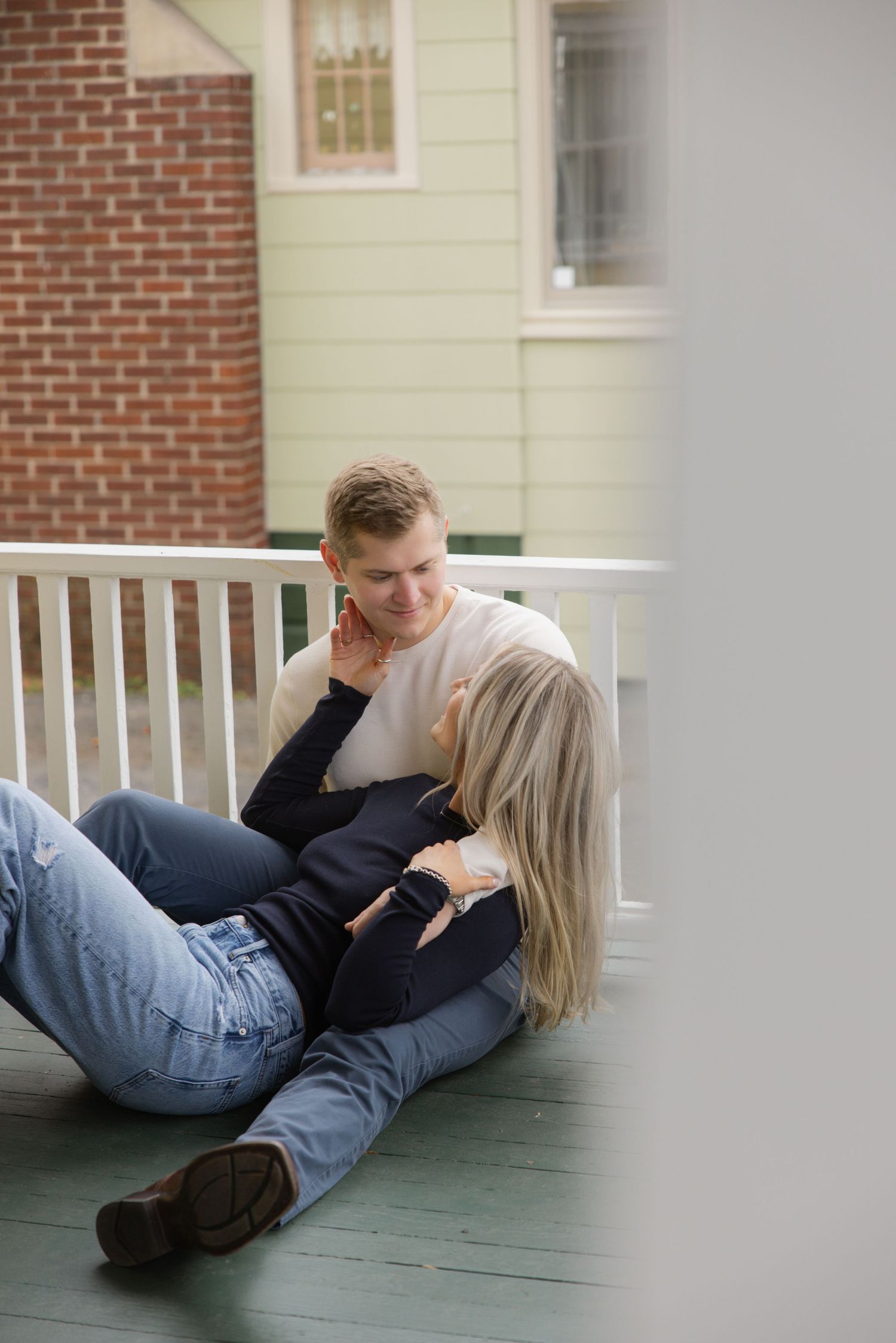 A couple relaxes together on their front porch in casual attire. Rochester NY home engagement photography