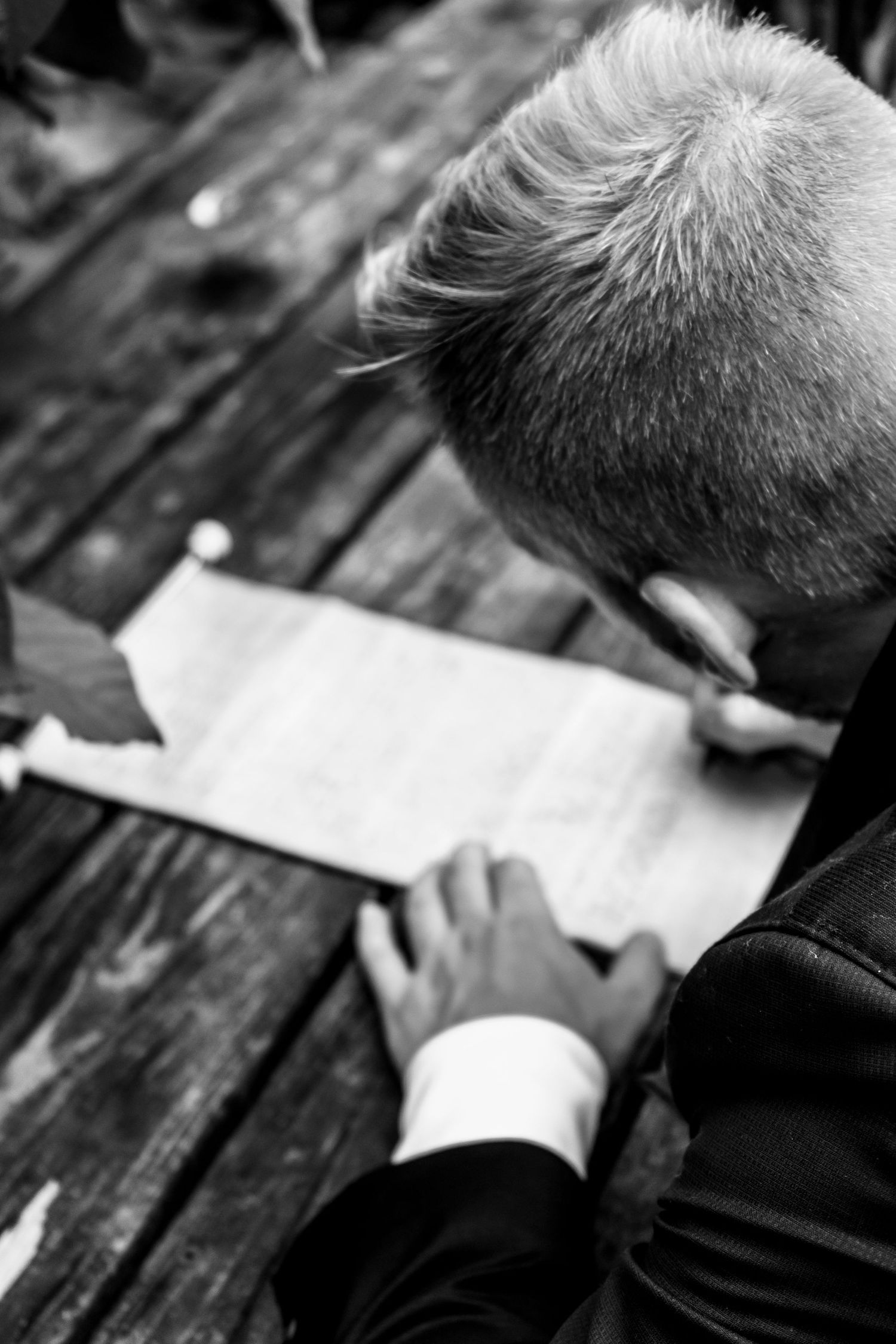 Person in formal attire reading a document at a wooden table, shown in black and white. Ithaca outdoor wedding photographer