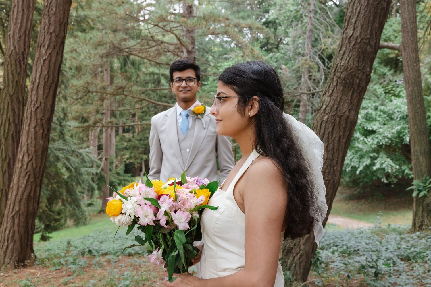 A couple in formal attire sharing joyful moments among tall pine trees.  Rochester conservatory elopement photographer