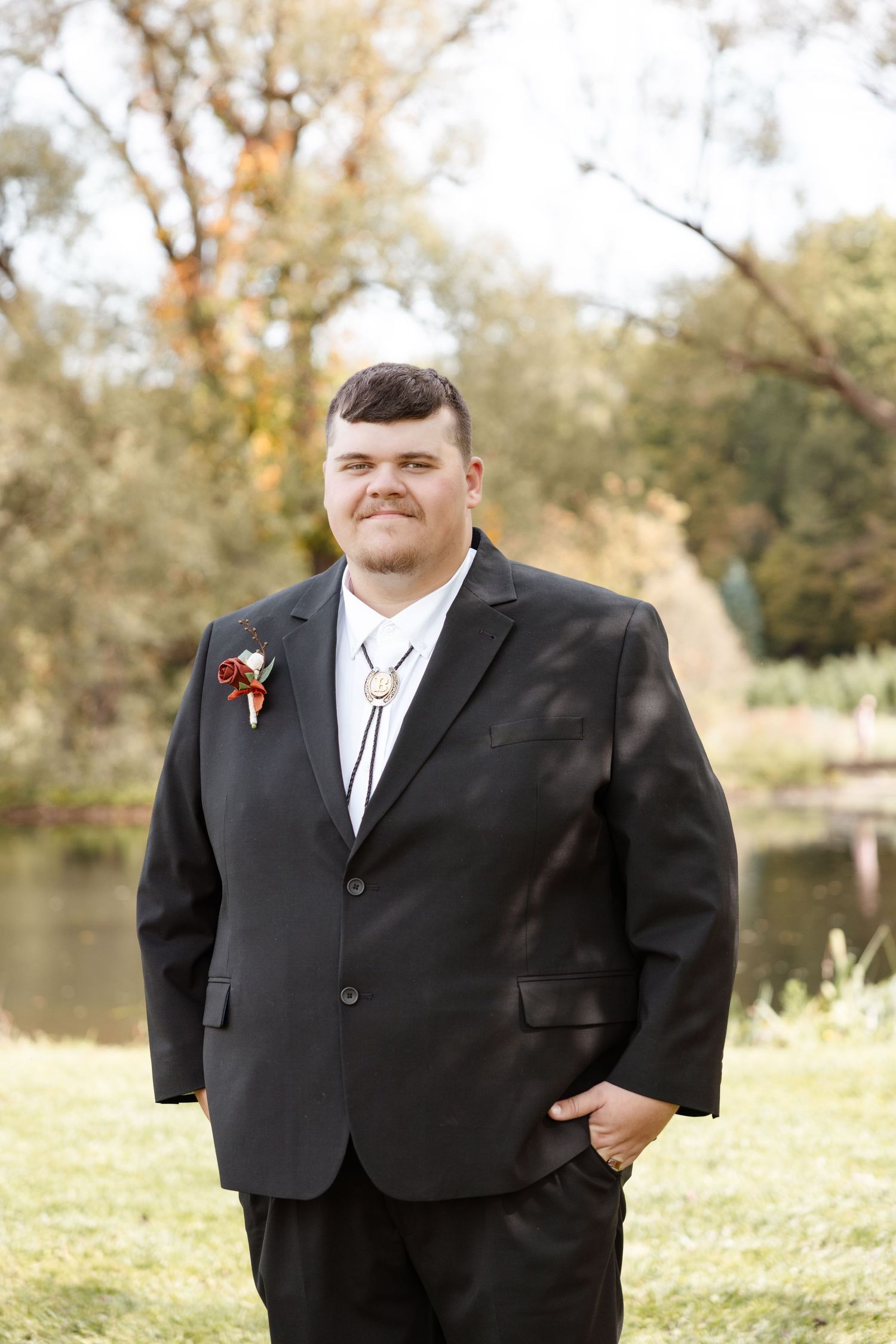 A groom in a black suit poses for formal wedding portraits in a park setting. wedding photographer Syracuse