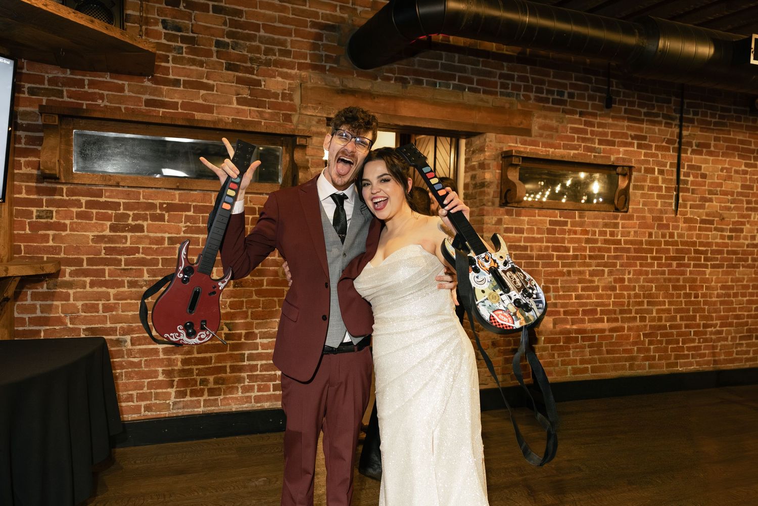 A bride and groom pose together in a rustic setting with brick walls and wooden beams.