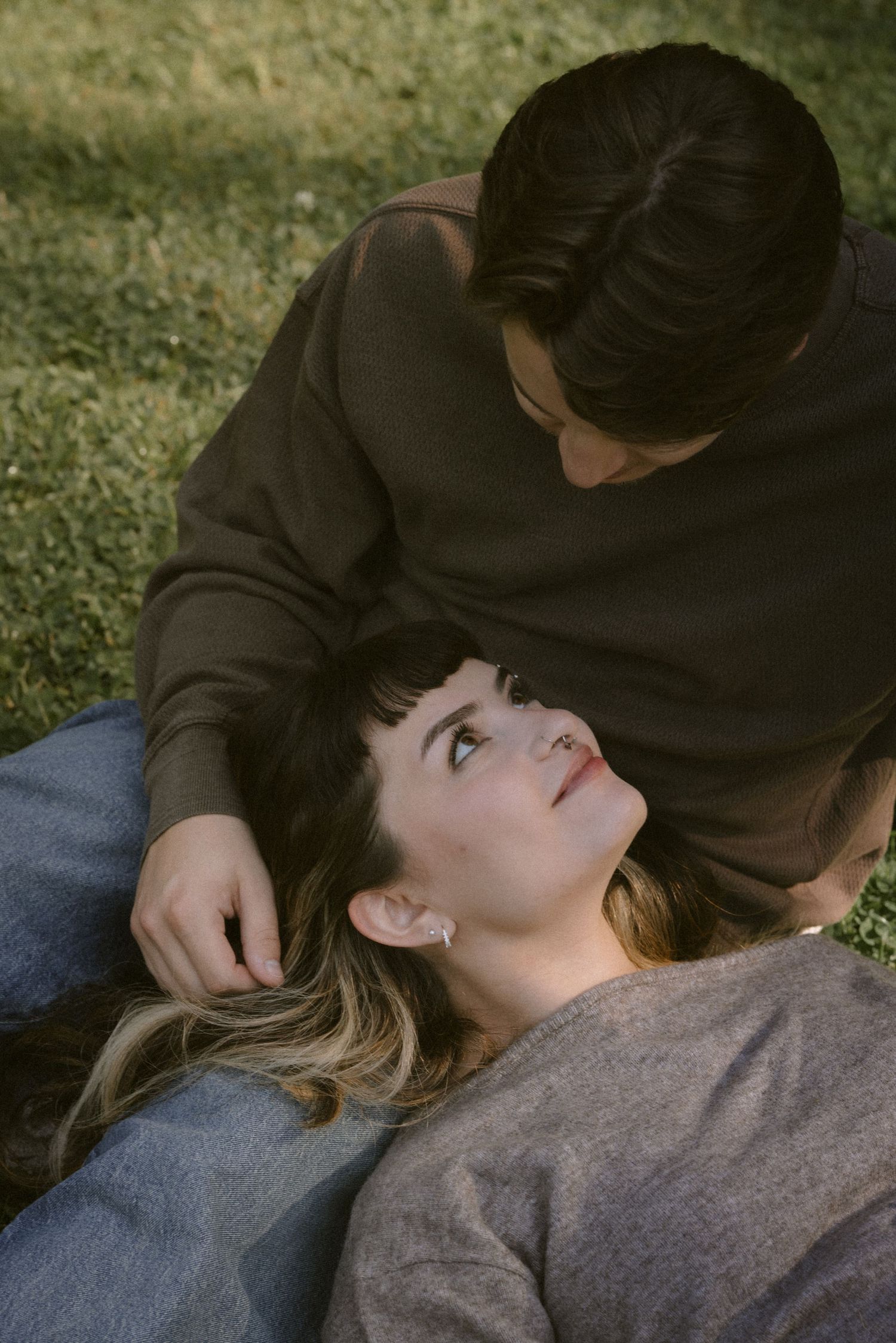An intimate moment captured between two people laying in grass outdoors. Rochester NY documentary engagement photography