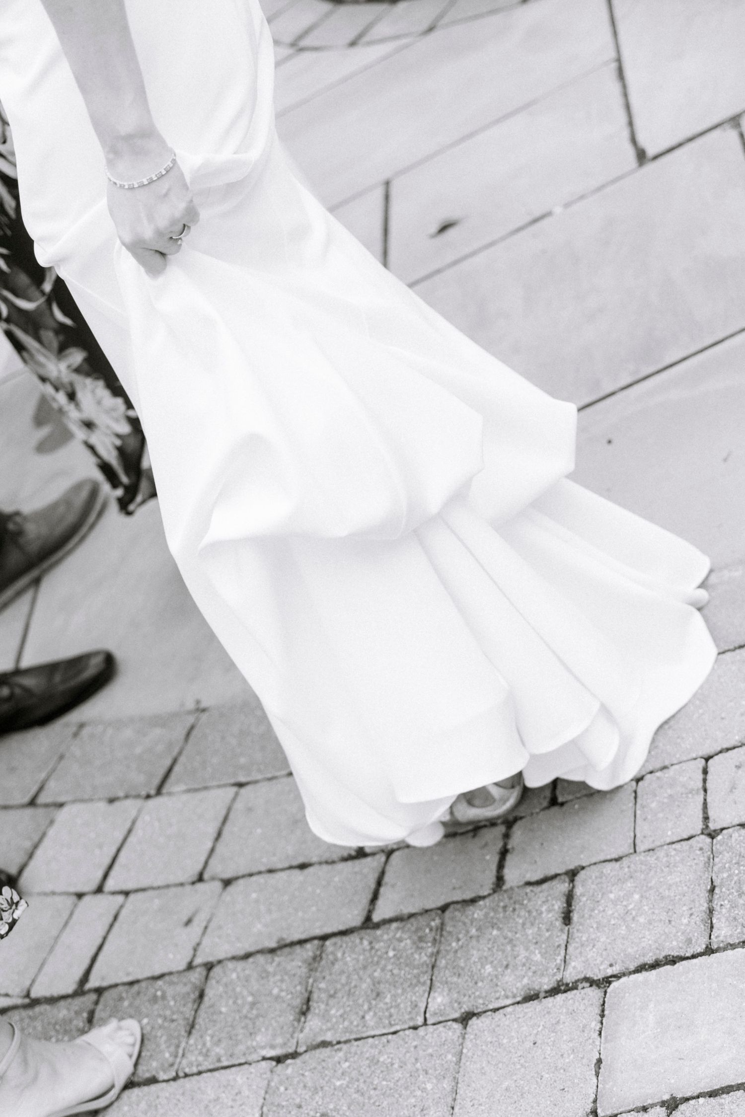 Close-up view of a white wedding dress hem and shoes on stone pavement. Rochester NY documentary wedding photography