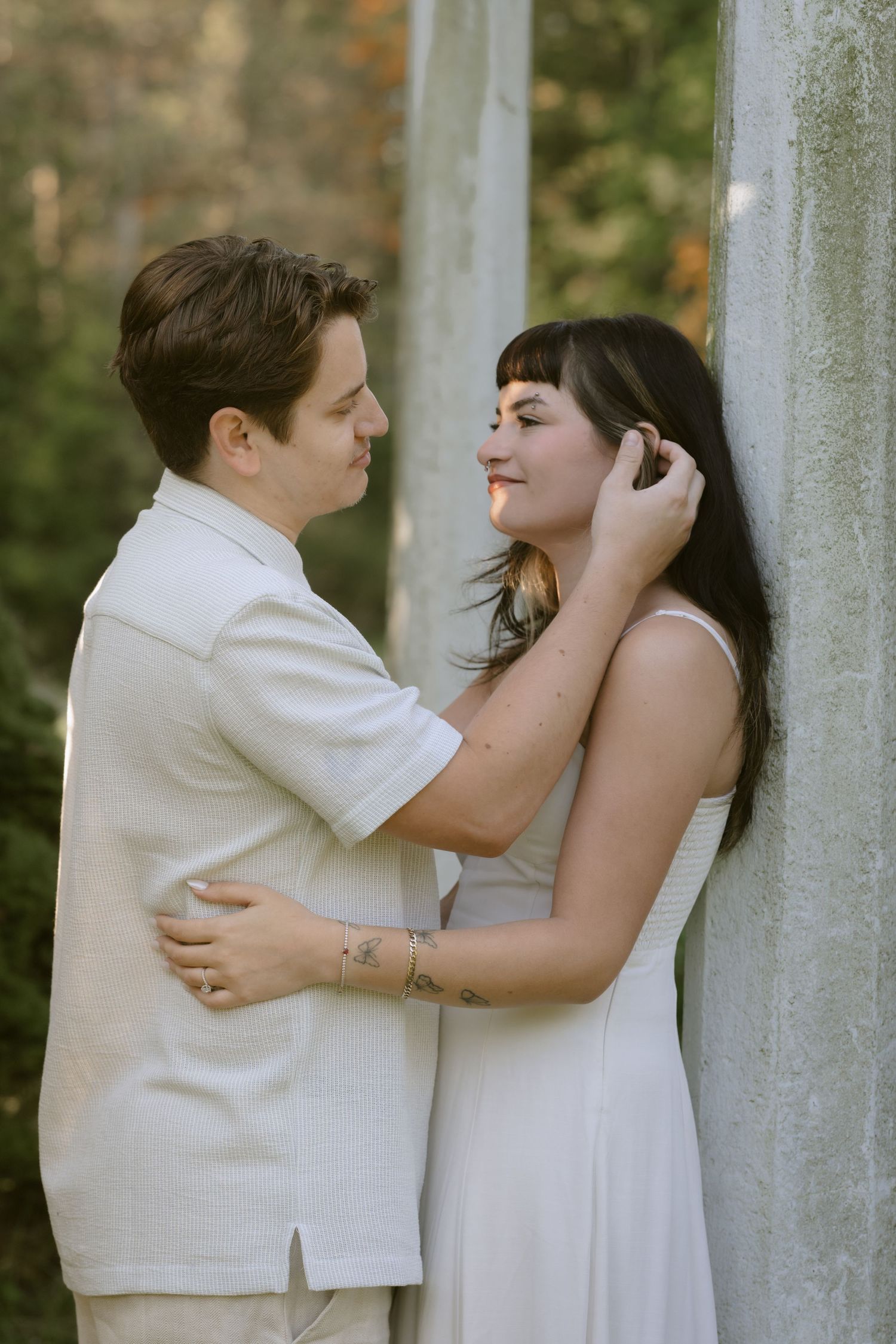 Intimate moment between two people in white attire near stone columns during a photoshoot. Rochester NY authentic engagement photography