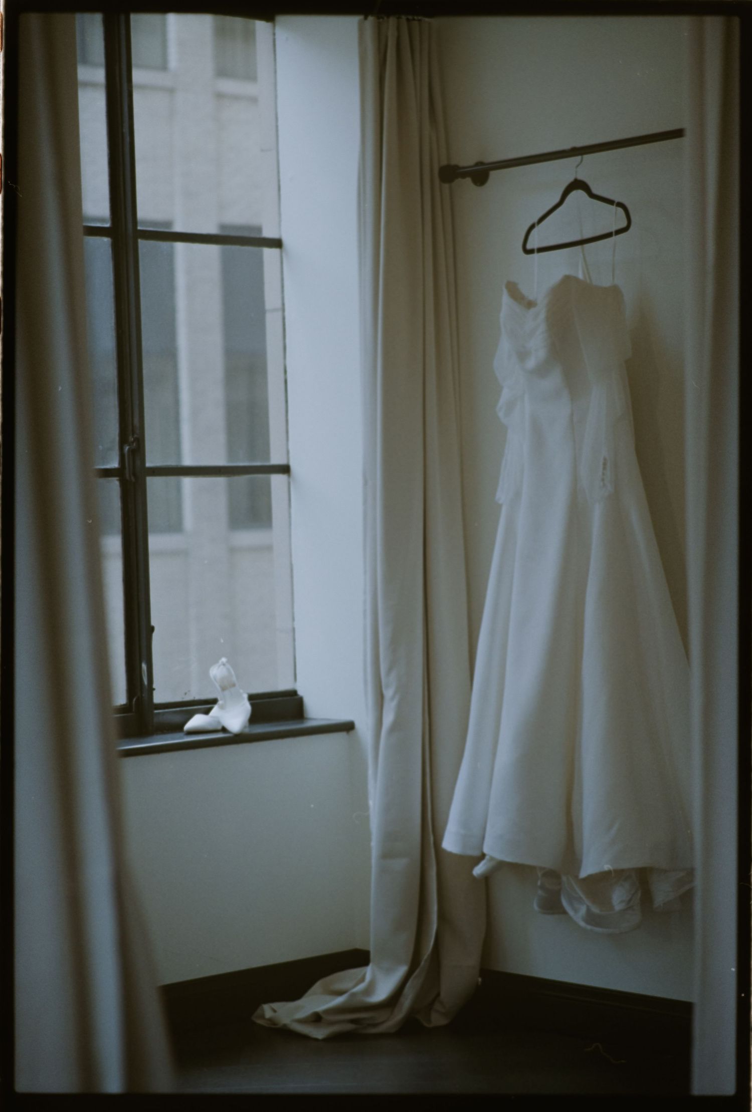 Wedding dress hanging on display near a window in a minimalist room.