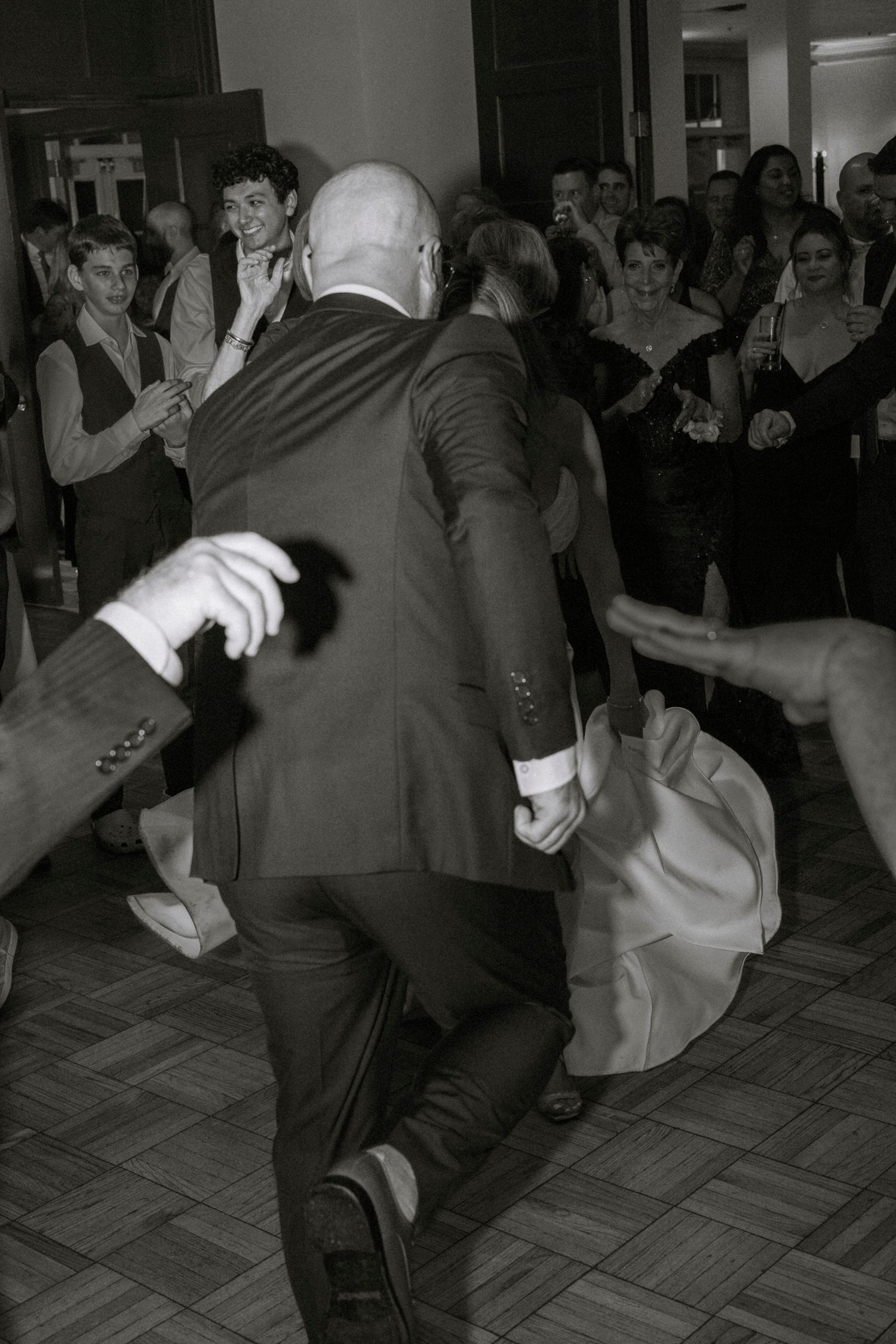 Energetic group dancing at an indoor celebration event. Rochester NY documentary wedding photography