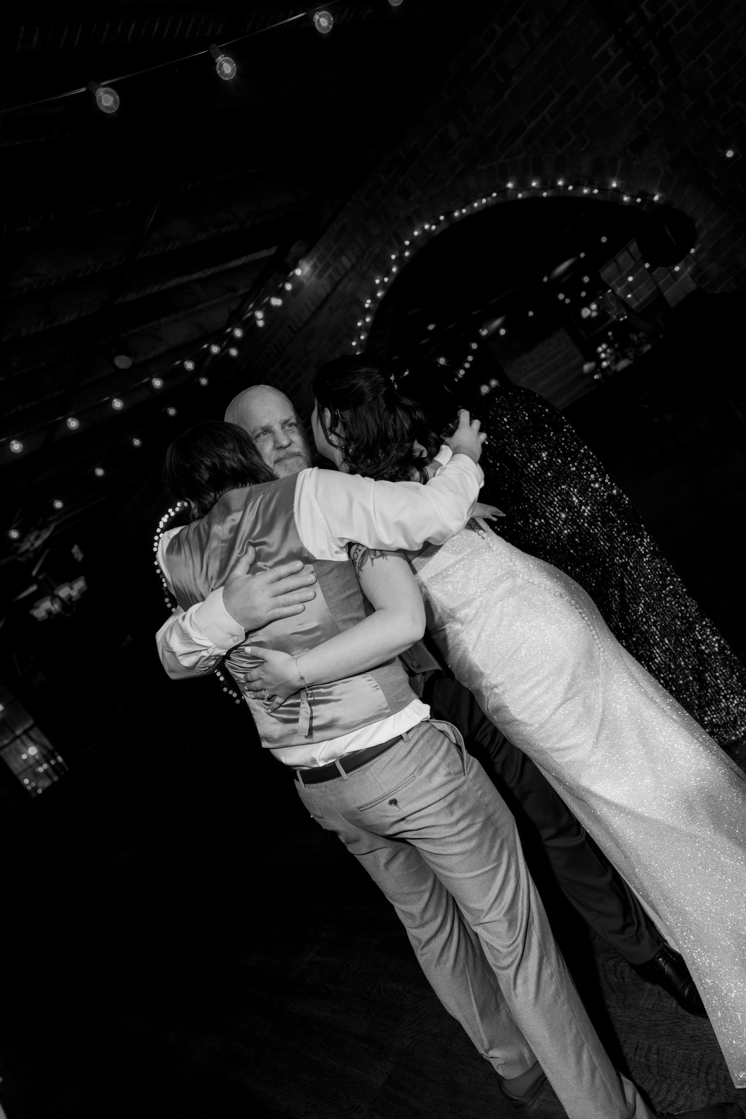 Black and white photo of a bride and groom sharing a group hug on the dance floor at their wedding reception.