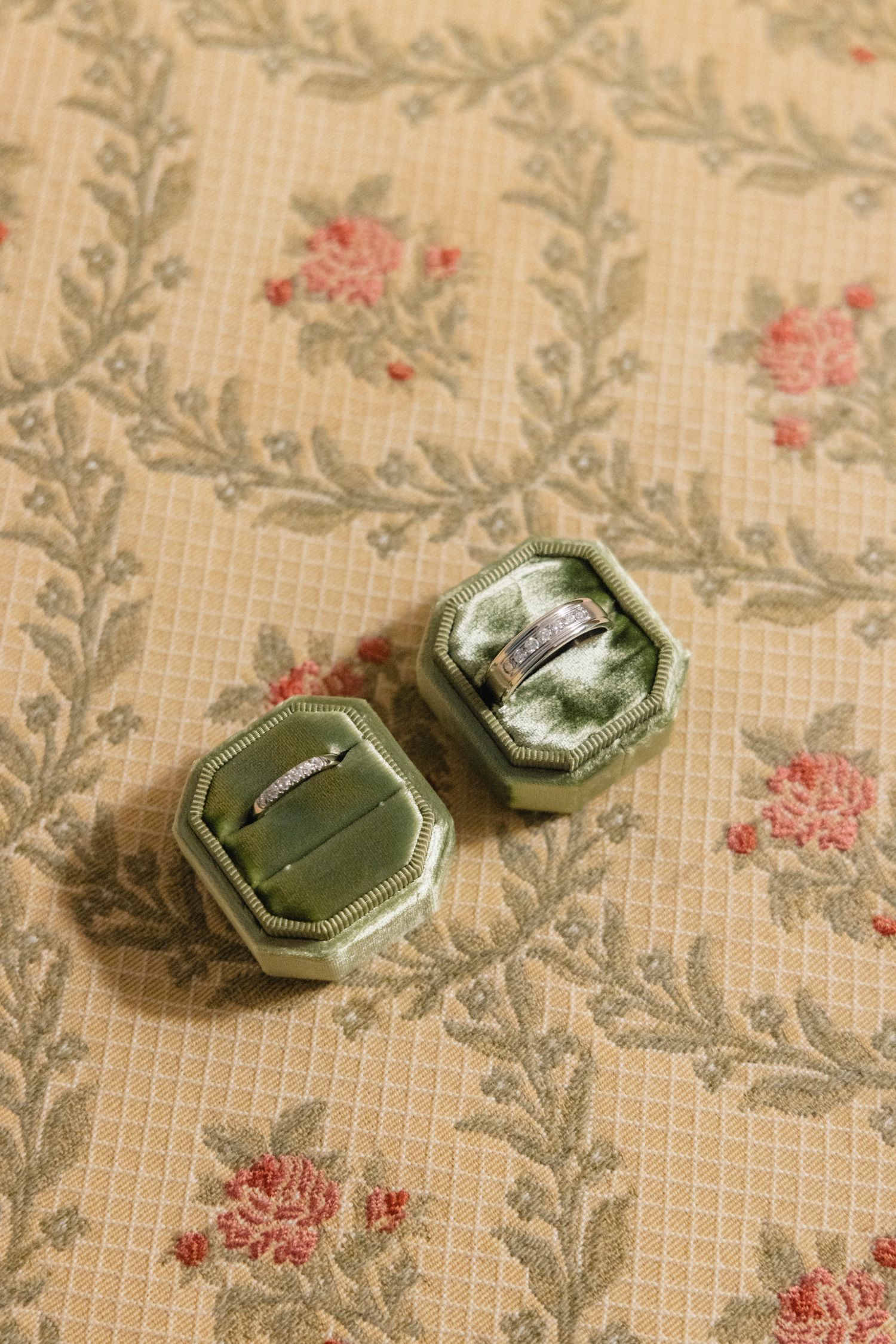 Vintage-style engagement rings displayed on a delicate floral patterned fabric background. Documentary wedding photography